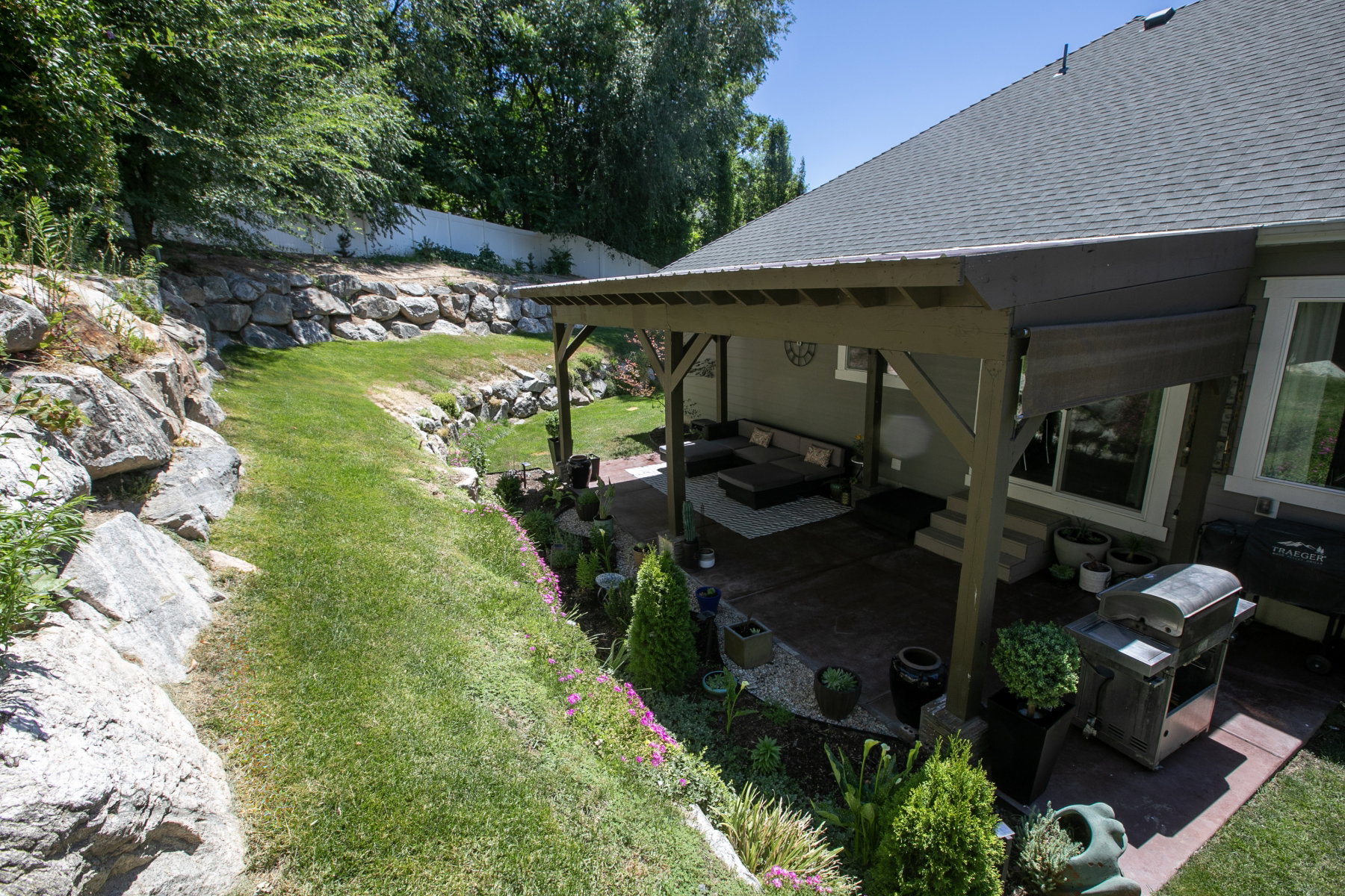 Expansive terraced backyard featuring natural rock retaining walls, a manicured lawn, and a covered patio with a wood-frame pergola