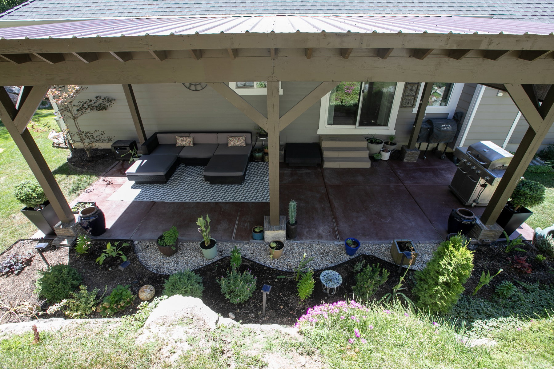 Covered patio with stained concrete flooring, featuring a pergola structure and a built-in planter with decorative rock and plantings