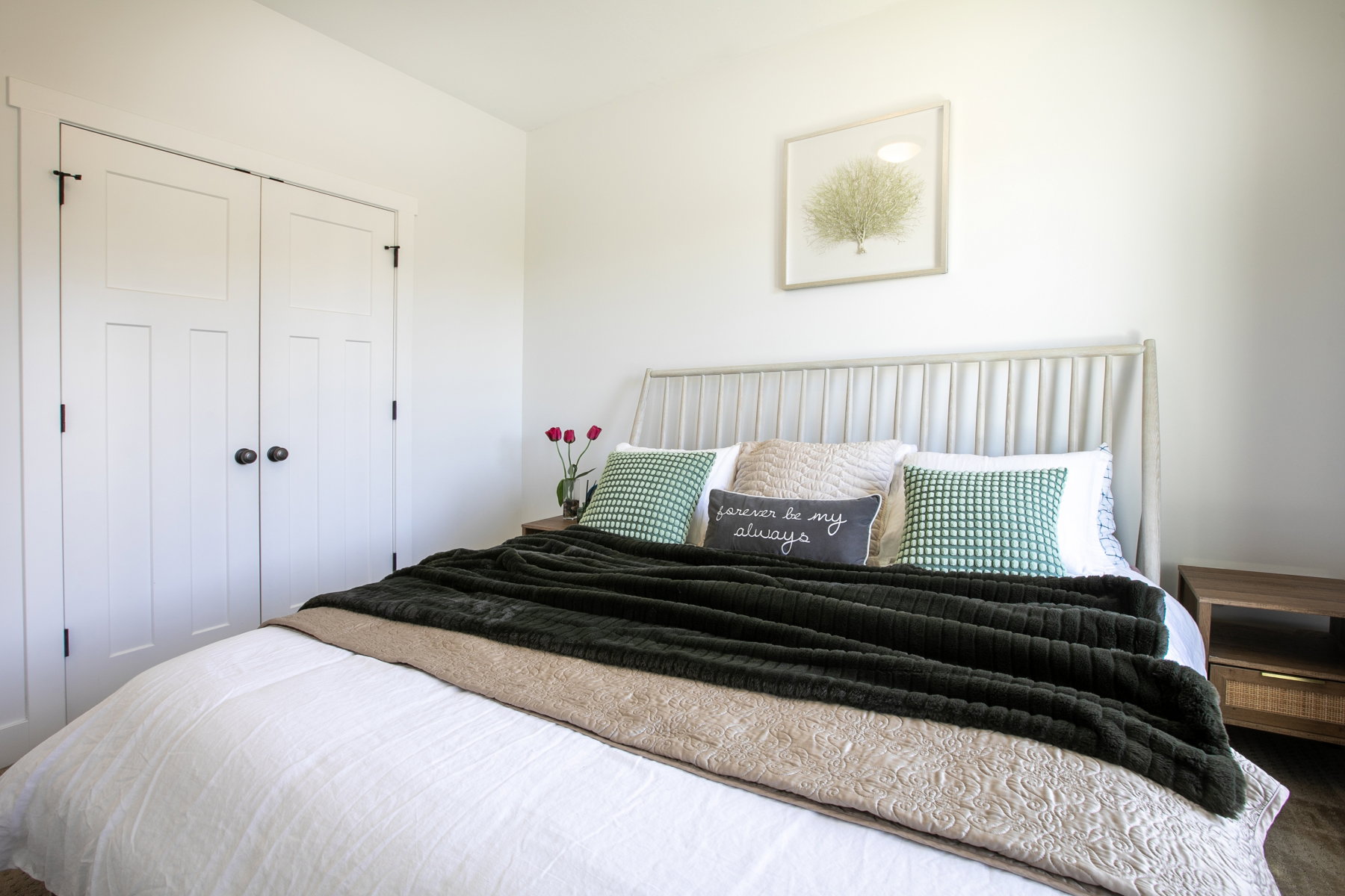 White paneled closet doors with dark hardware, a light-toned headboard, and a wood-finish side table
