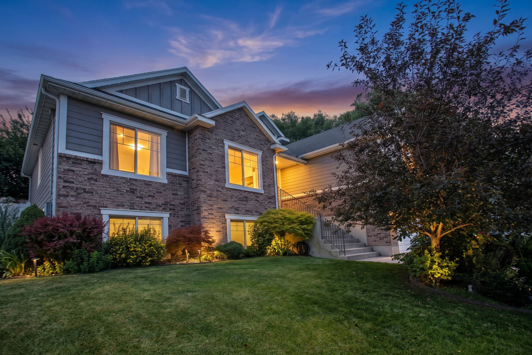 Split-level residence featuring a stone and siding facade, multi-pane windows, mature landscaping, and exterior lighting