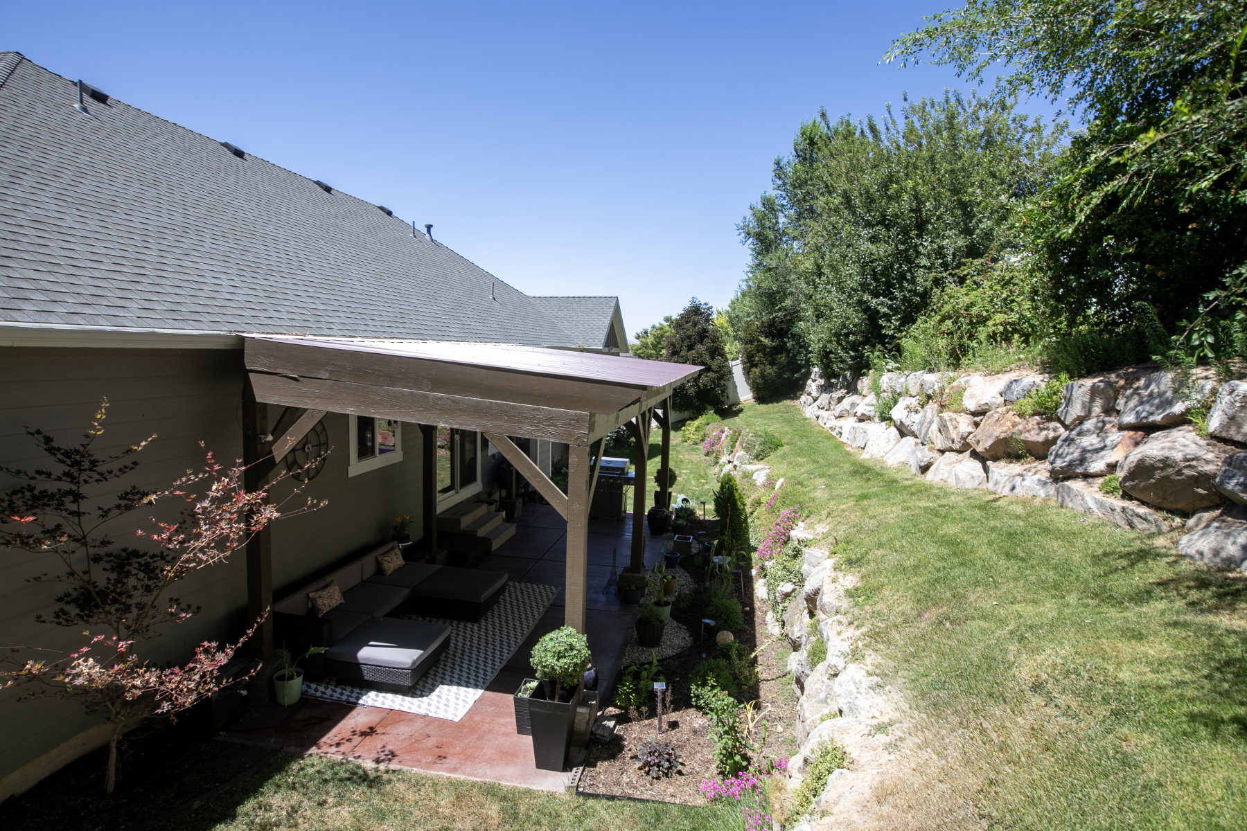 Covered patio with a patterned outdoor rug, an expansive rock retaining wall, and a sloped grassy area