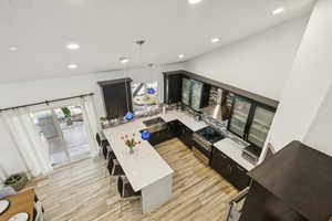 Kitchen featuring dark cabinetry, decorative light fixtures, a kitchen breakfast bar, high end range, and a peninsula