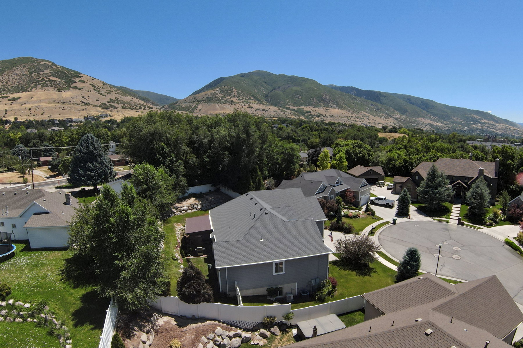 Aerial perspective showcasing a residential property with a gray exterior and a shingled roof, surrounded by mature trees