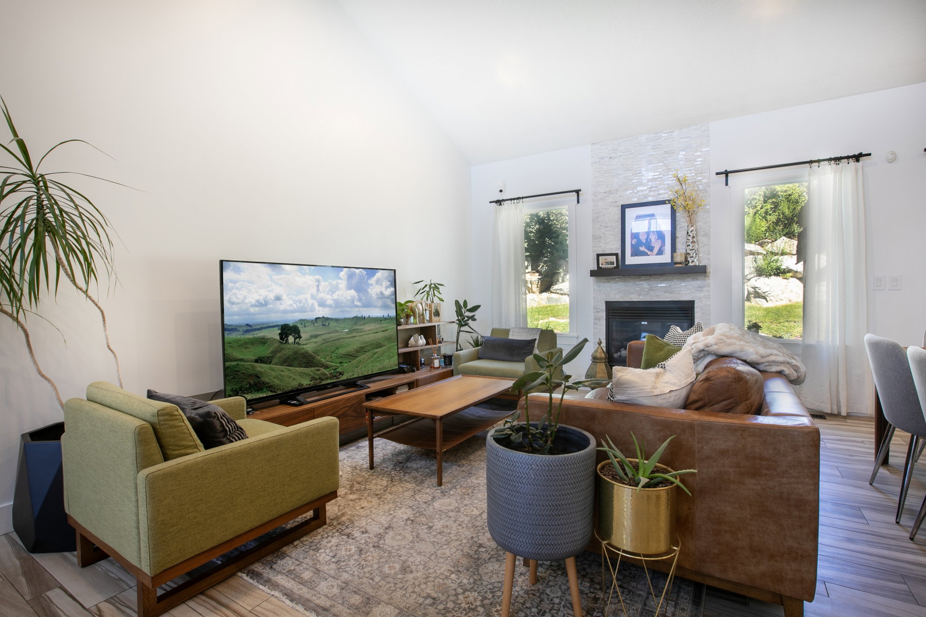 Spacious living area featuring a vaulted ceiling, wood-finish flooring, and a fireplace with a stacked stone facade and dark wood mantel
