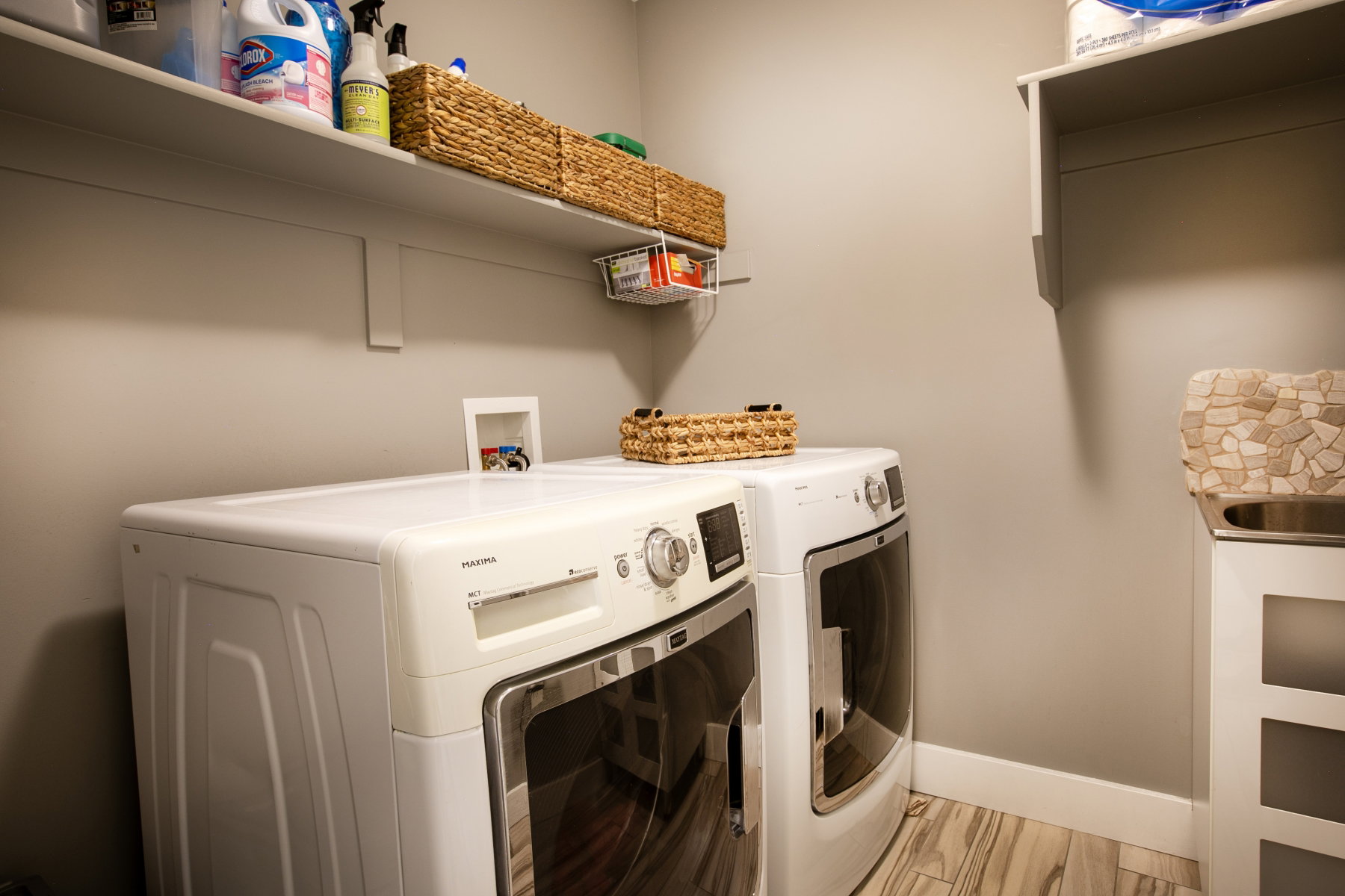 Dedicated laundry area featuring wood-finish flooring, light neutral wall paint, white baseboards, and built-in shelving for storage