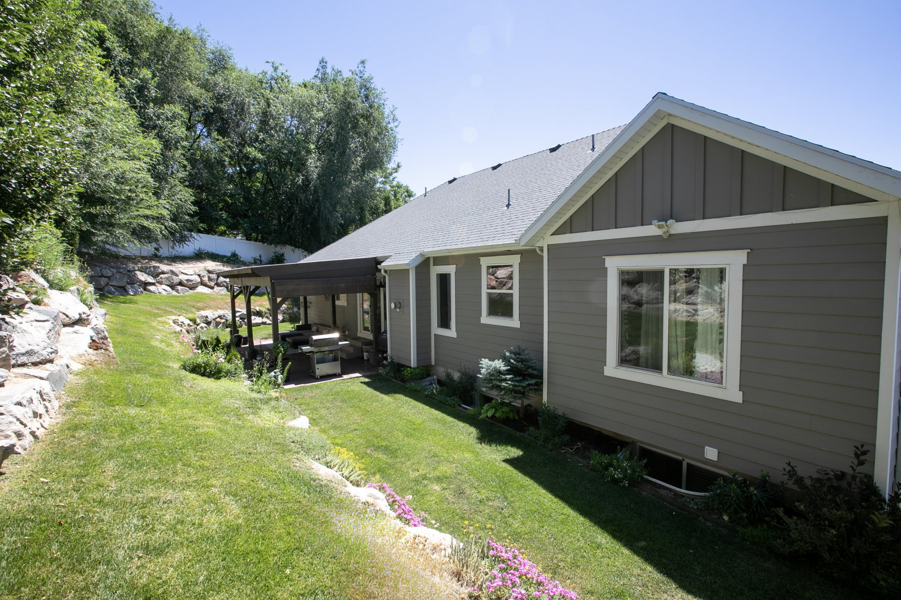 Exterior featuring gray siding with white trim, a gabled roofline, and a covered patio structure
