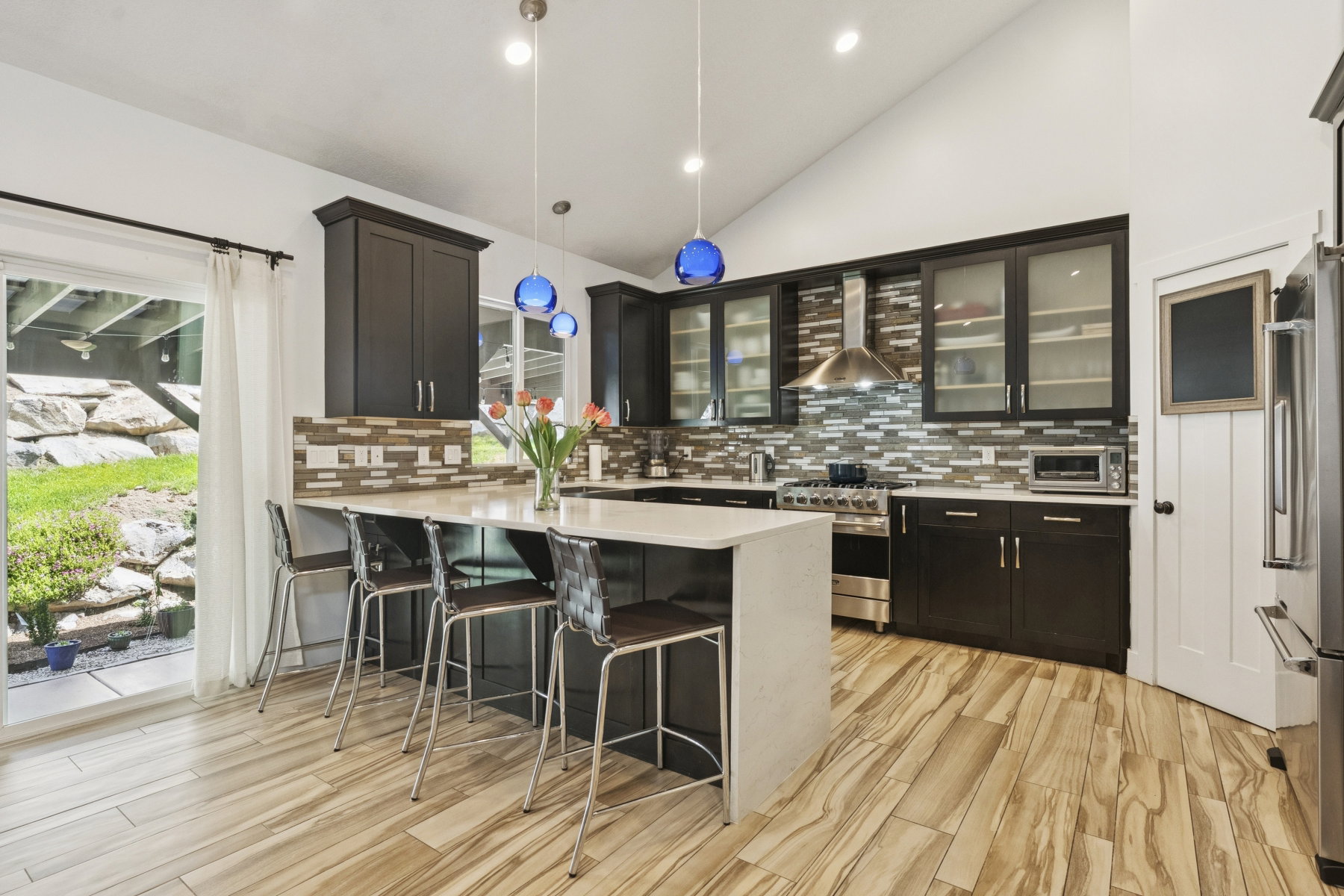 Kitchen featuring vaulted ceiling, decorative light fixtures, a peninsula, a breakfast bar area, and light wood-type flooring
