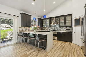 Kitchen featuring vaulted ceiling, decorative light fixtures, a peninsula, a breakfast bar area, and light wood-type flooring