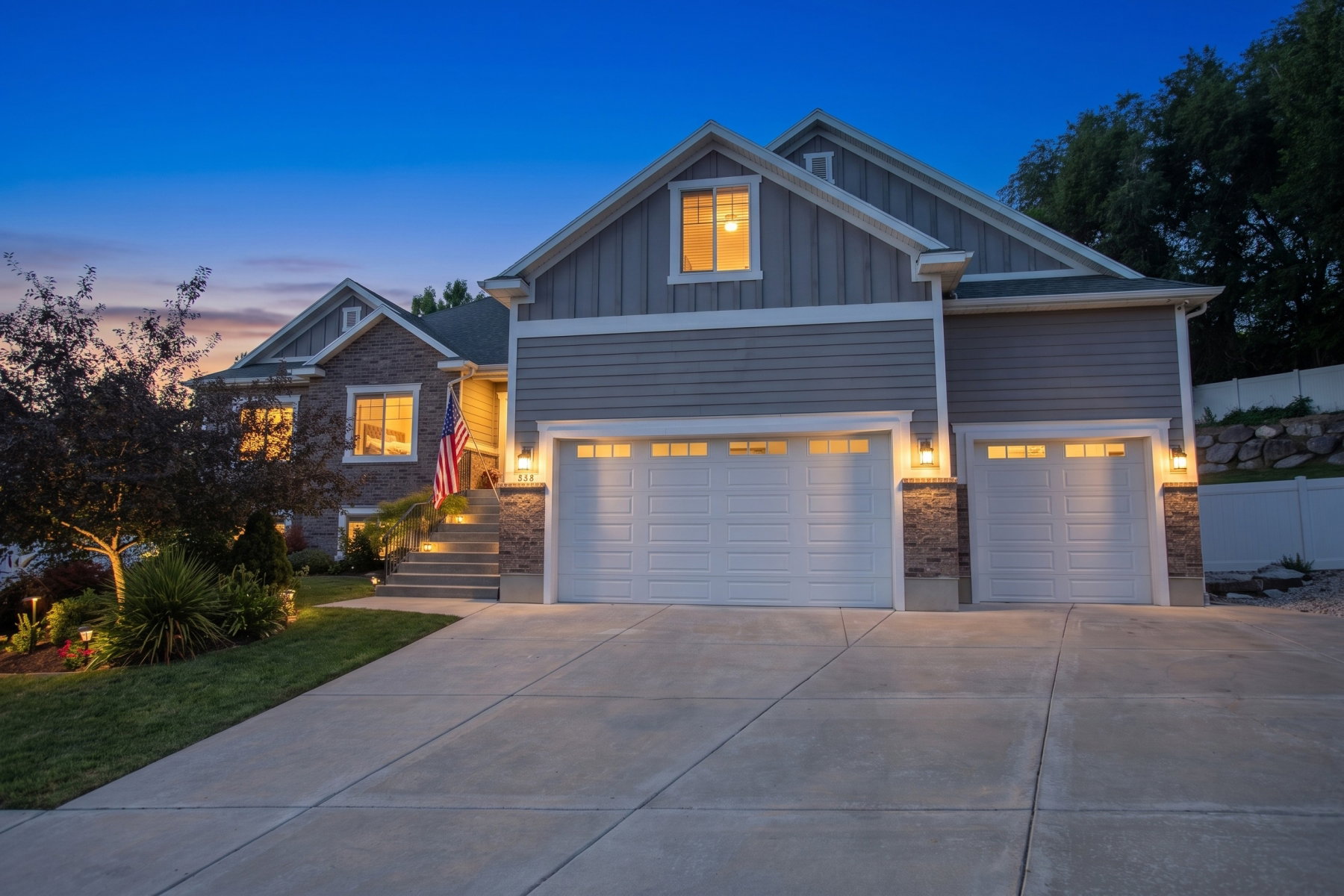 Exterior featuring stone and siding finishes, a concrete driveway, dual garage doors with integrated windows, a stepped entryway, and landscape lighting