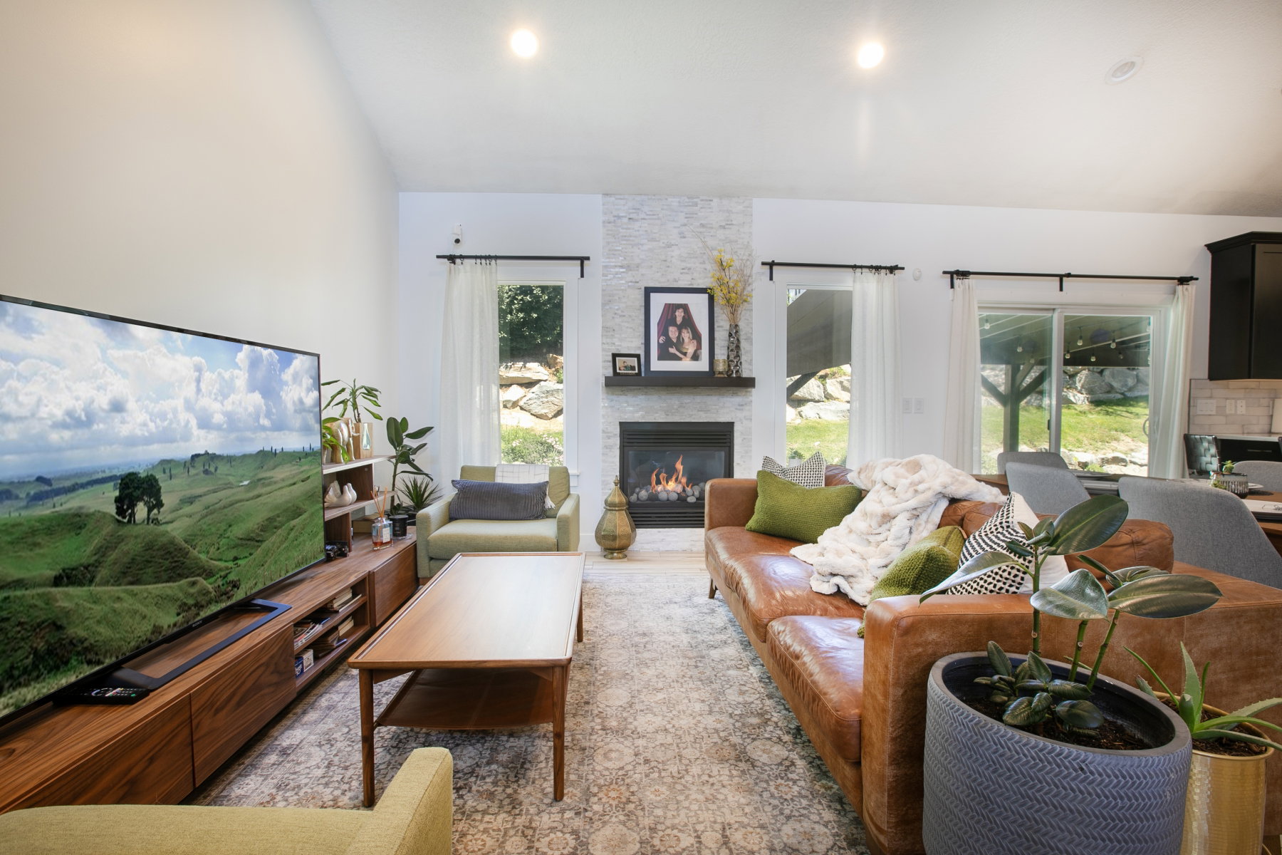 Inviting living space featuring a stone-clad fireplace with a dark wood mantel, recessed lighting, and a large window providing natural light