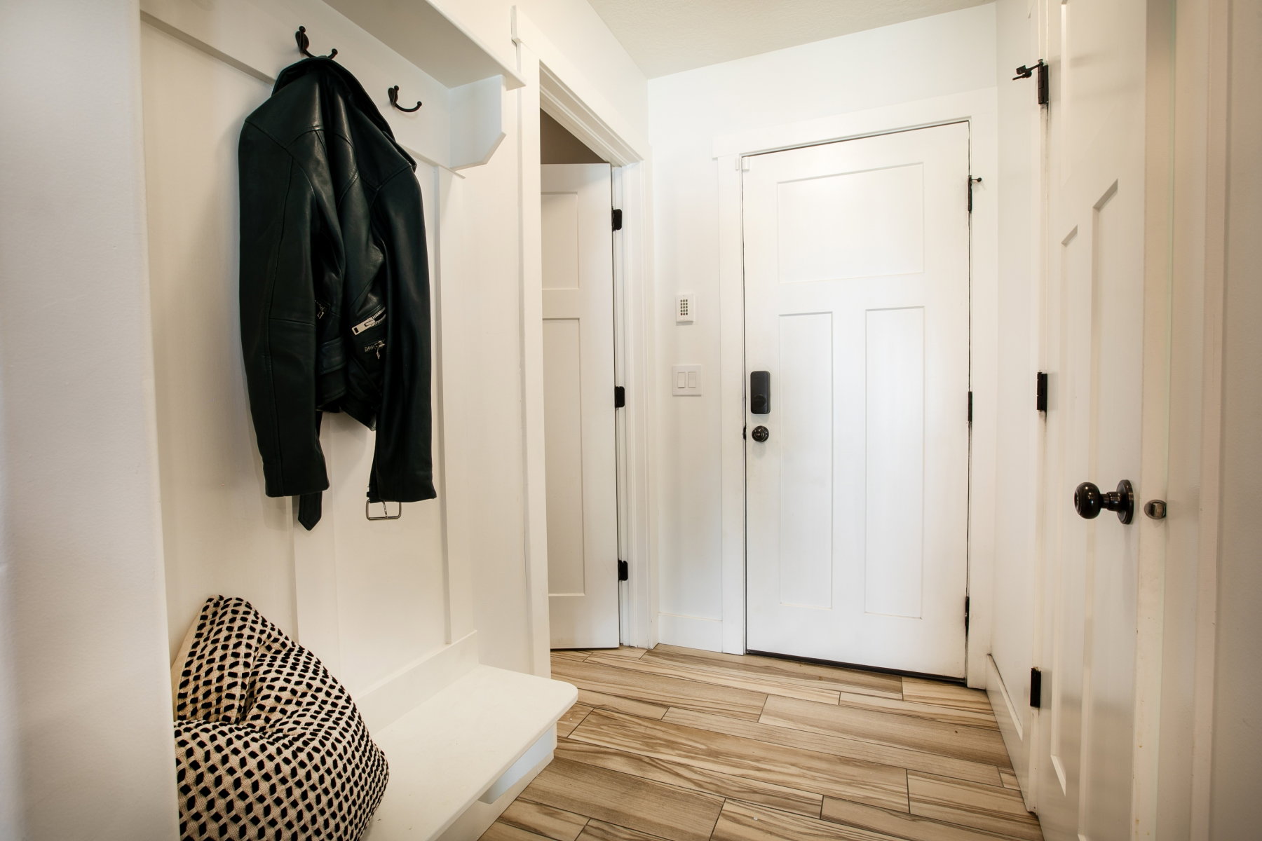 Entryway featuring light wood-finish flooring, white panel doors with black hardware, and a built-in bench with wall hooks