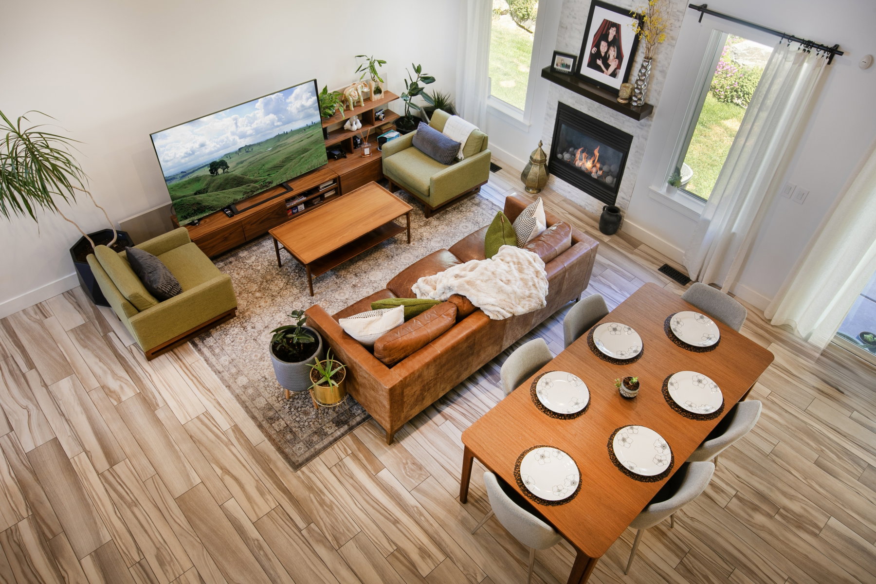 Open-concept living area featuring wood-finish flooring, a contemporary fireplace with a white tile surround and wood mantel, large windows with white curtains, and a dedicated dining space