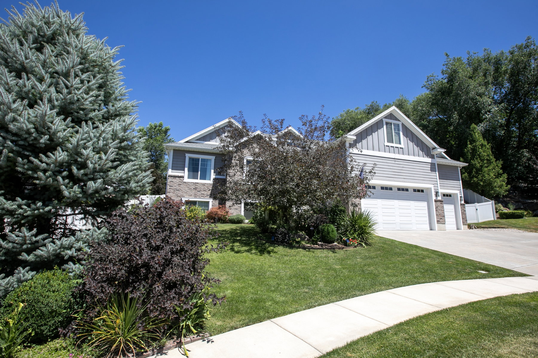 Contemporary gray siding and stone exterior featuring multiple gables, a two-car garage, and a concrete driveway