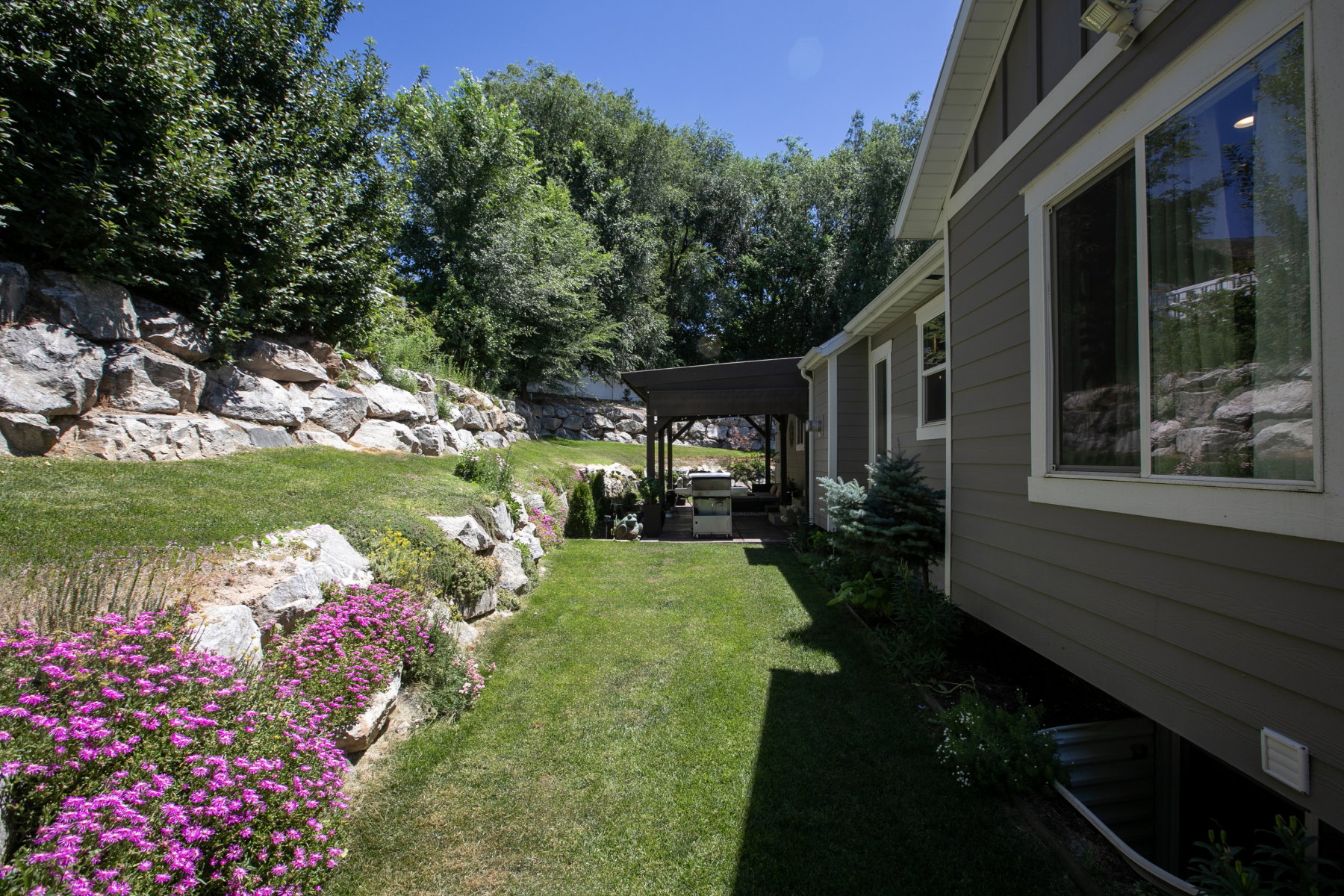 Expansive green lawn bordering a rock retaining wall with vibrant pink floral plantings