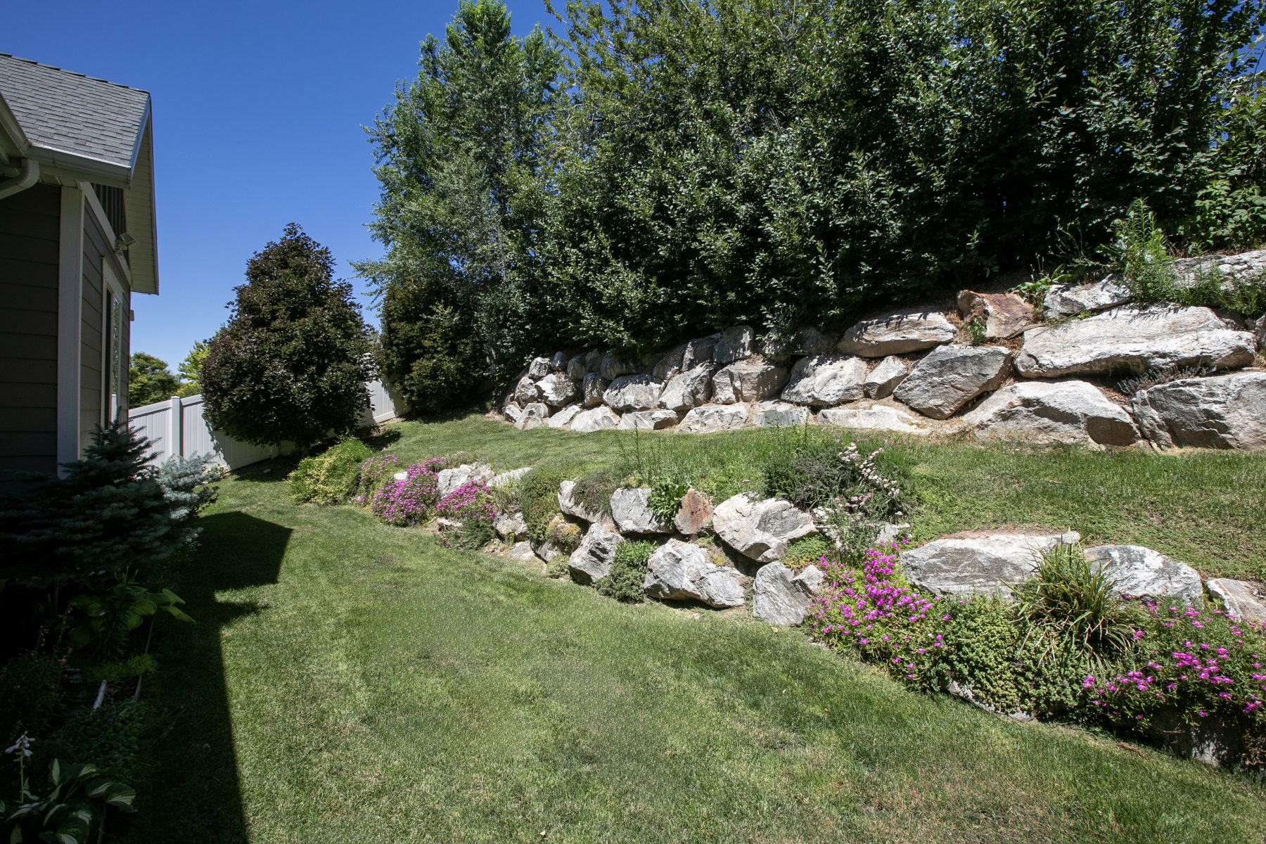 Tiered landscaping featuring a rock retaining wall, mature trees, and vibrant groundcover