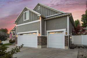 View of front of house with board and batten siding, driveway, a garage, and brick siding