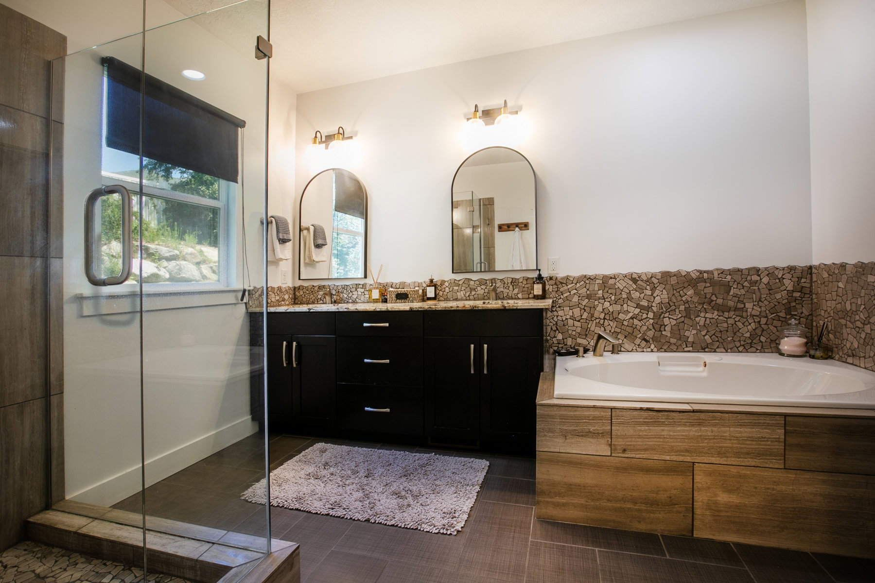 Spacious bathroom featuring a glass-enclosed shower, a double vanity with dark wood cabinetry and granite countertops, and a built-in jetted tub with wood-finish paneling
