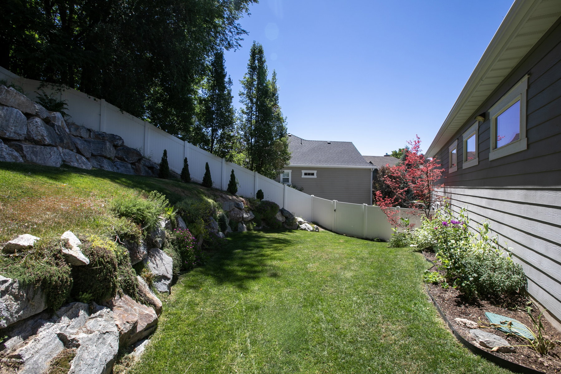 Expansive grassy side yard featuring a white privacy fence, natural rock landscaping, and mature trees