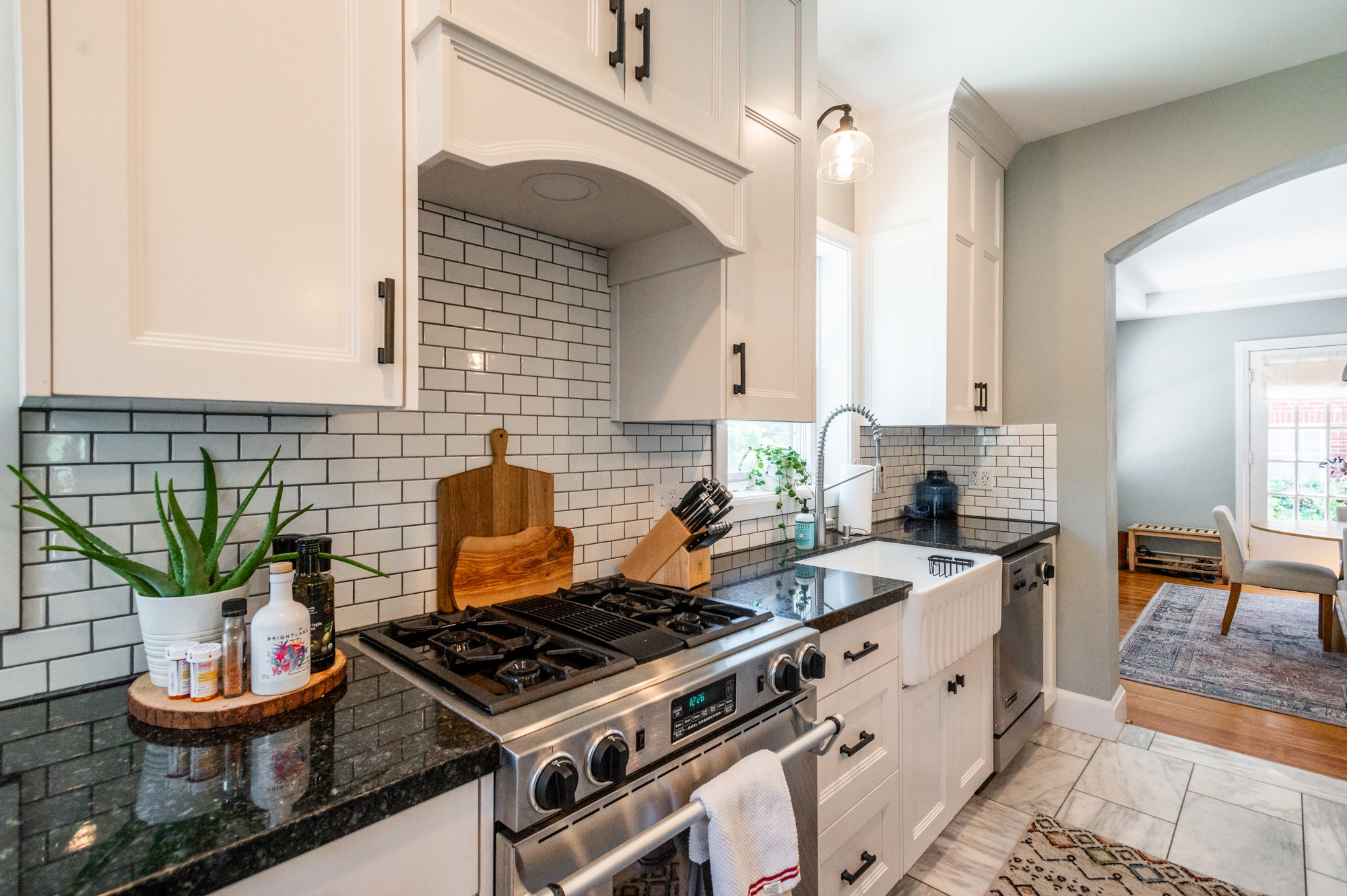 Kitchen featuring white shaker-style cabinetry, black hardware, subway tile backsplash, dark stone countertops, a stainless steel range, and a white farmhouse sink