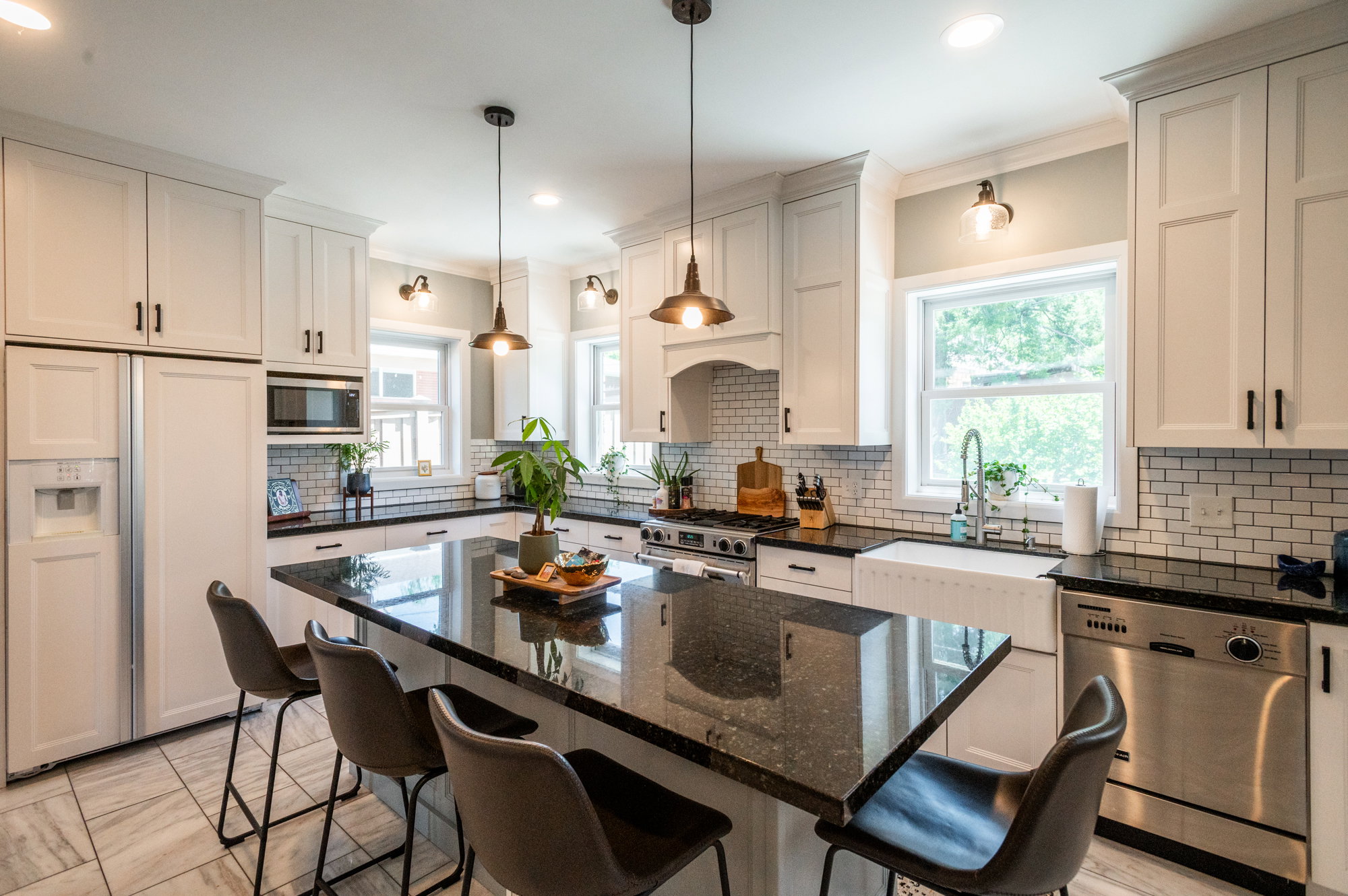 Modern kitchen featuring a large central island with seating, white shaker cabinetry, dark granite countertops, and a subway tile backsplash