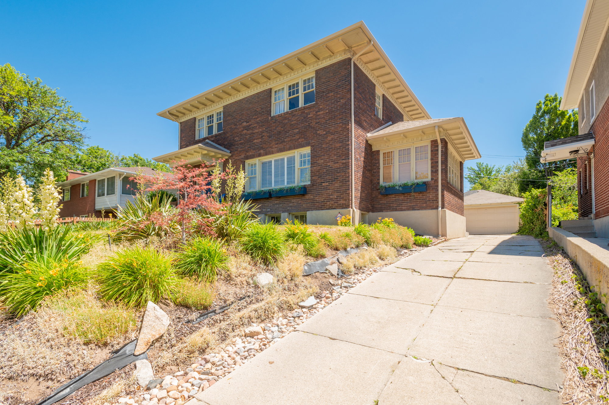 Brick exterior residence featuring a concrete driveway, a separate garage structure, and a sloped front yard with established landscaping