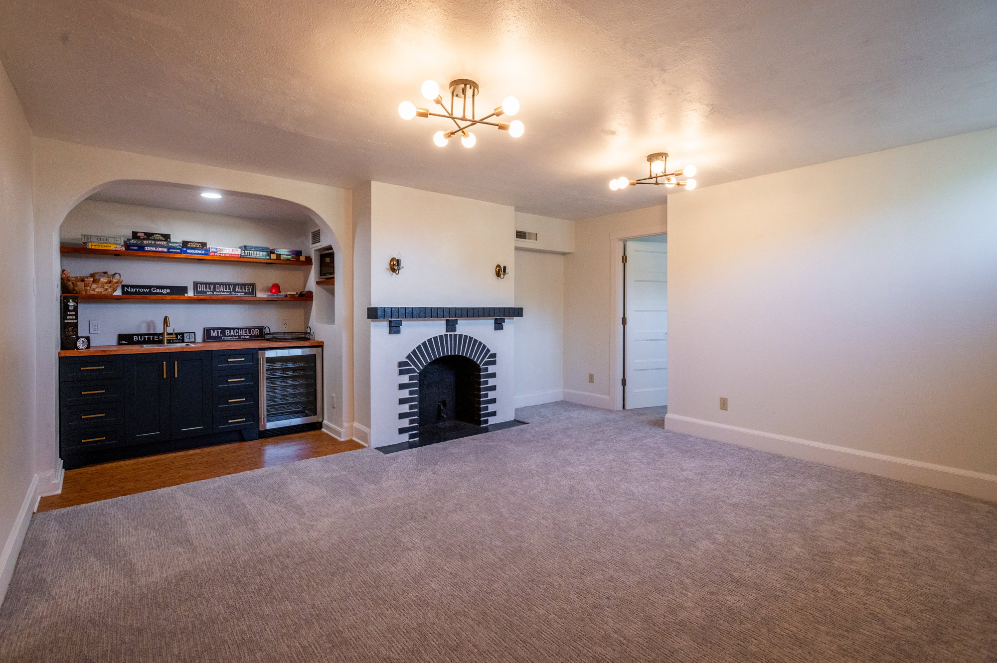 Spacious room featuring new carpeting, a fireplace with a black and white brick surround, and two modern ceiling light fixtures