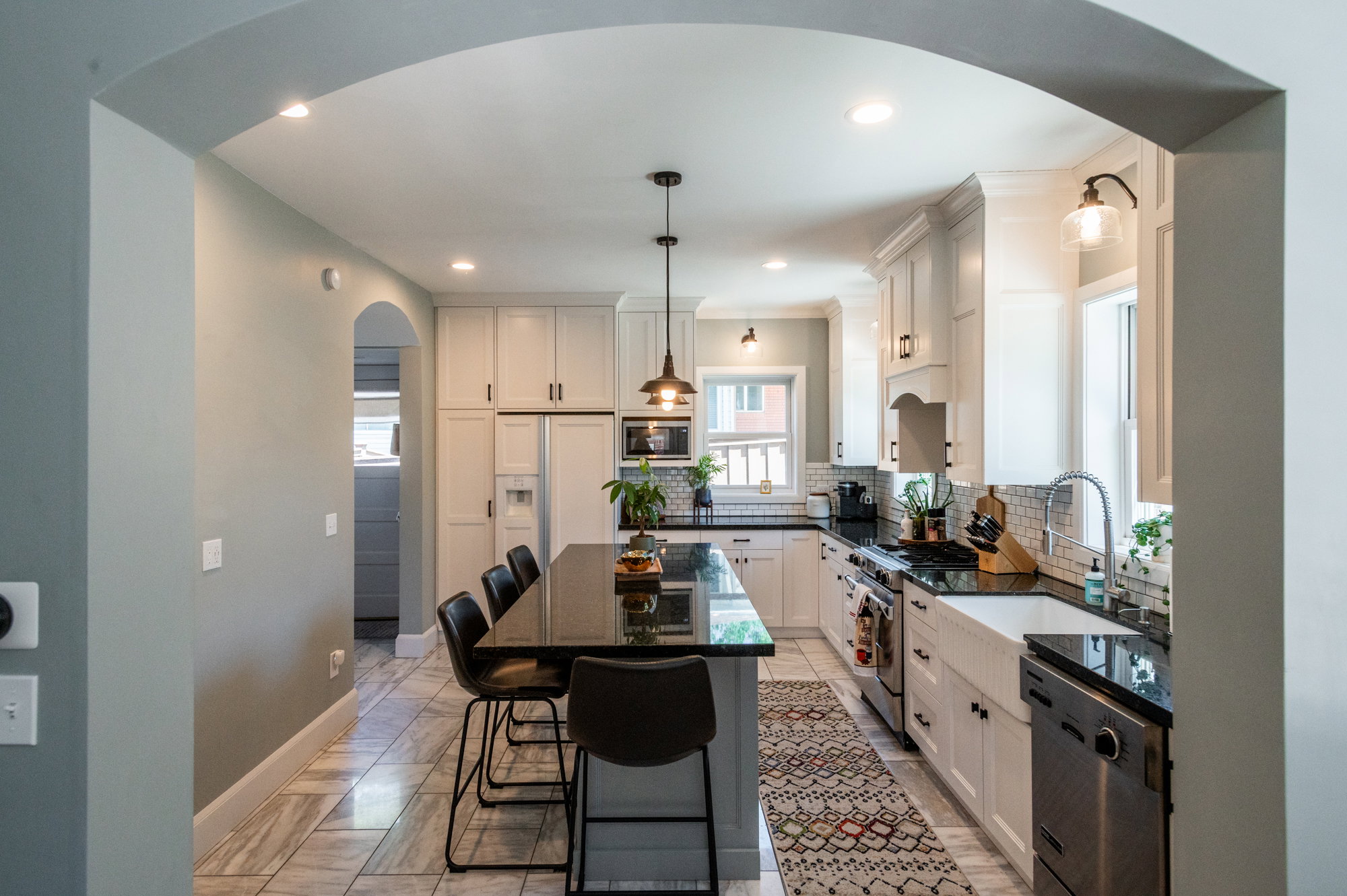Kitchen featuring a large central island with seating, white shaker-style cabinetry, dark countertops, a farmhouse sink, and stainless steel appliances