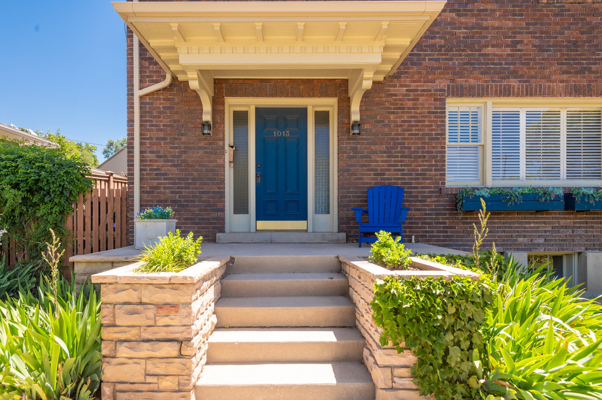 Brick exterior featuring a covered entry porch with decorative corbels, a vibrant blue front door, and a multi-tiered concrete staircase