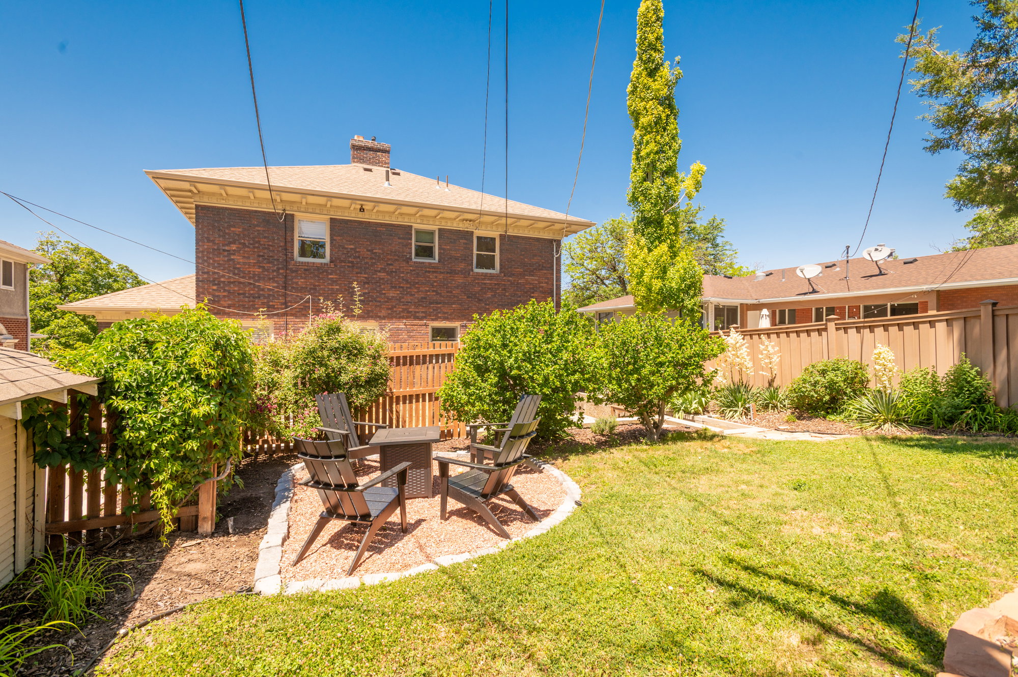 Expansive backyard featuring a central lawn area, brick exterior, wood fencing, and a dedicated gravel patio space