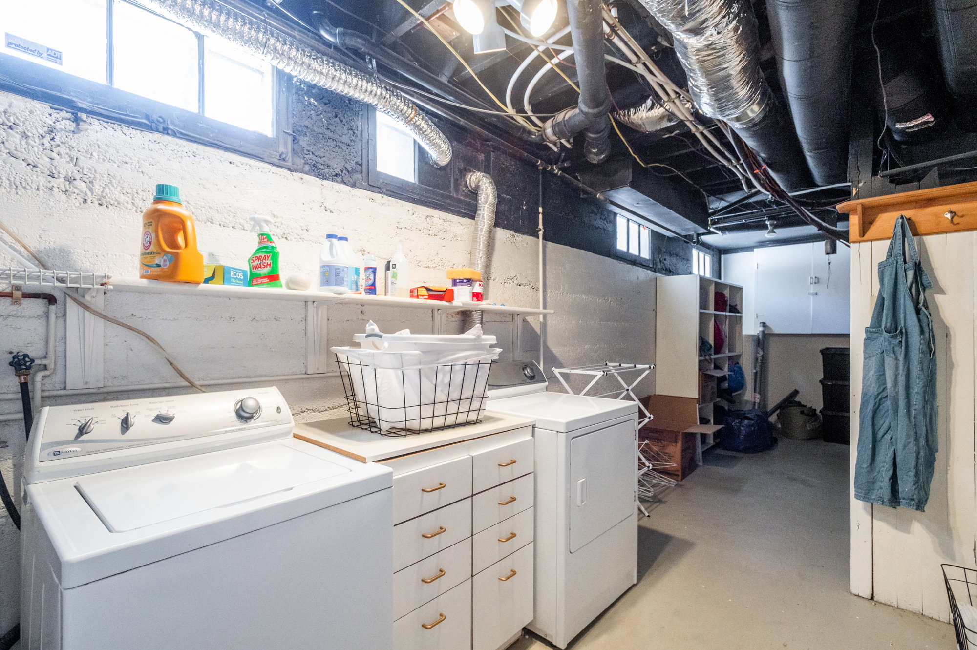 Dedicated laundry area featuring a washer and dryer, built-in cabinetry with gold-tone hardware, a wall-mounted shelving unit, and a utility sink