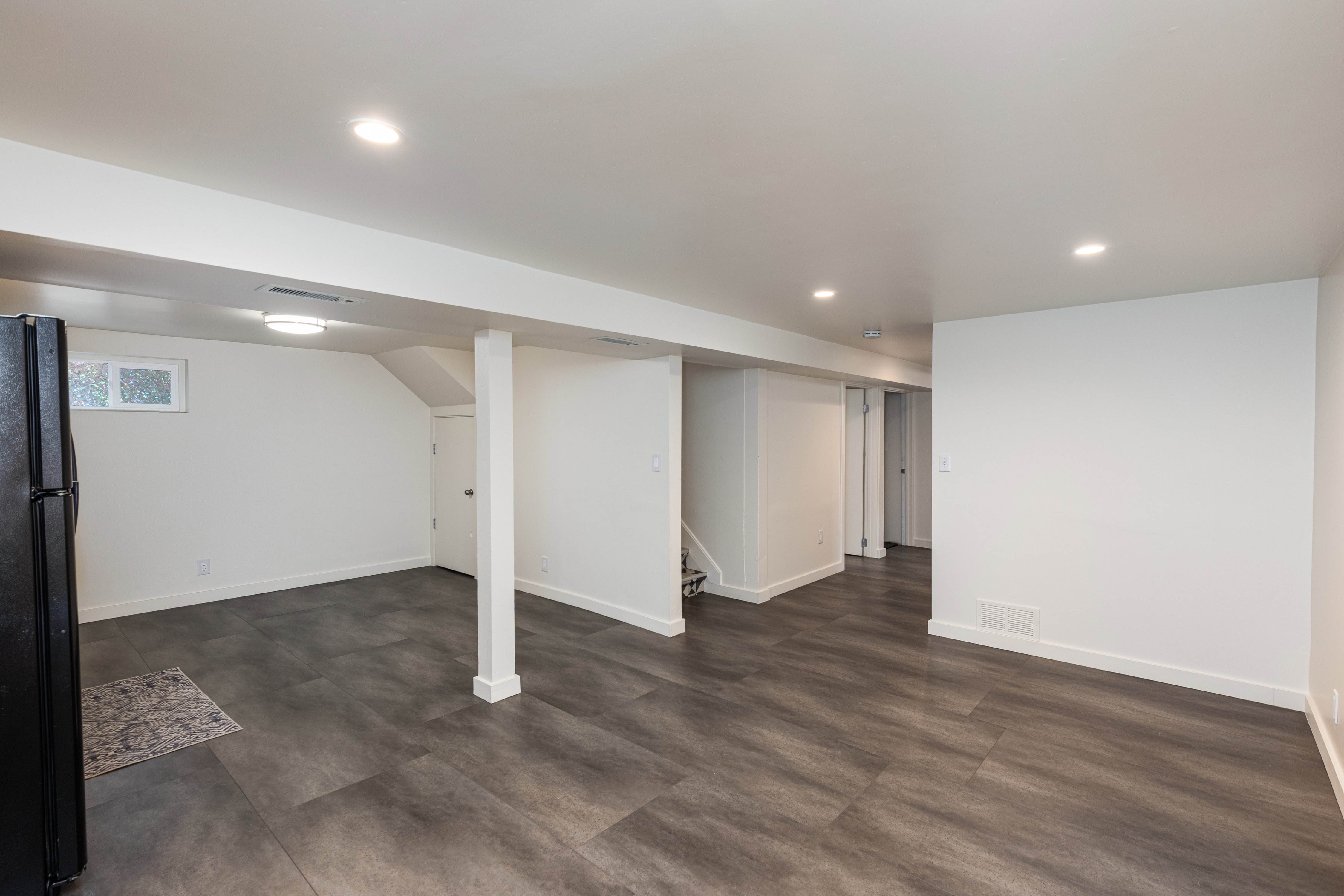 Spacious room featuring wood-finish flooring, recessed lighting, white walls, and a window for natural light