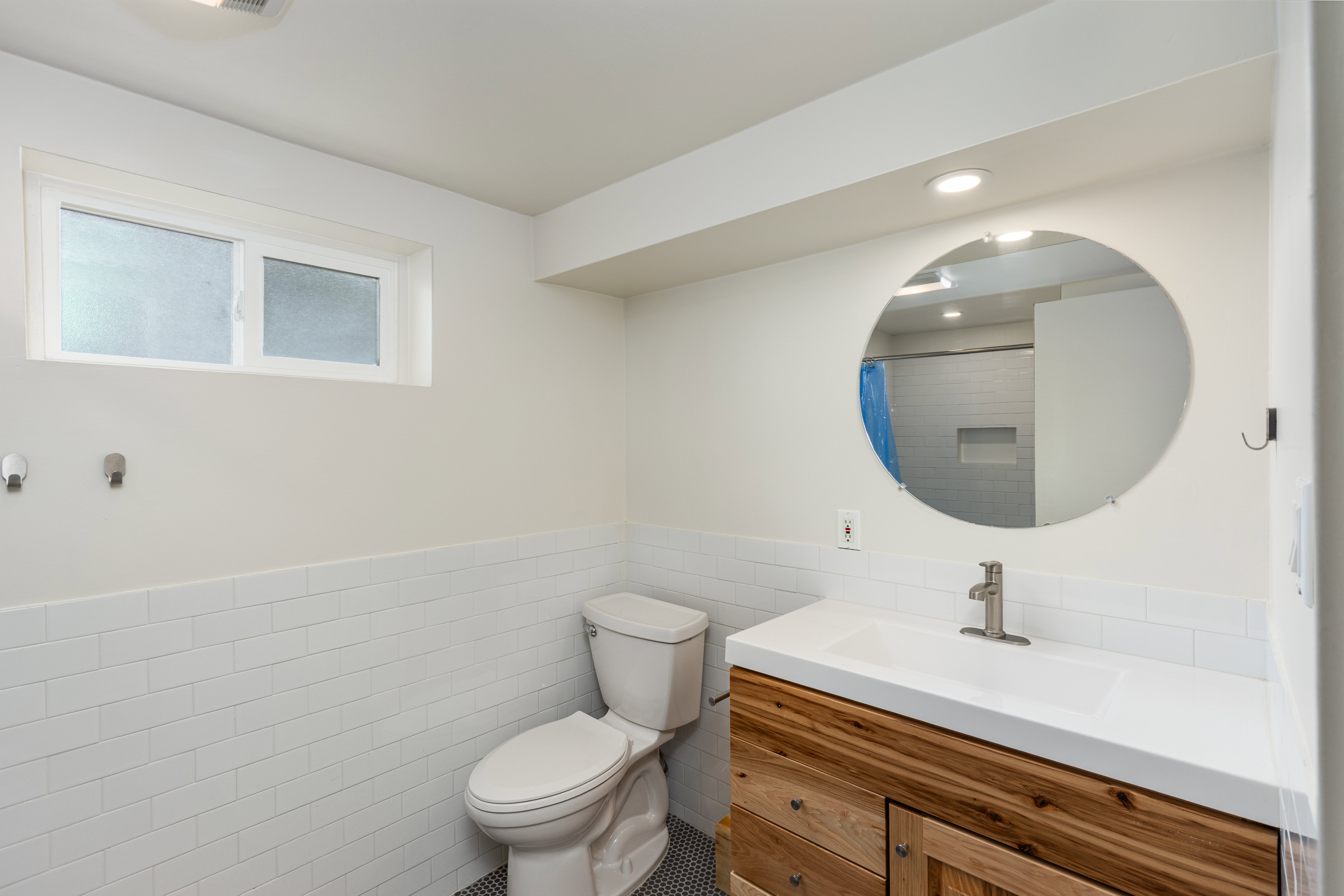 Bathroom featuring a natural wood-finish vanity with a white countertop and integrated sink, a circular wall mirror, and a toilet