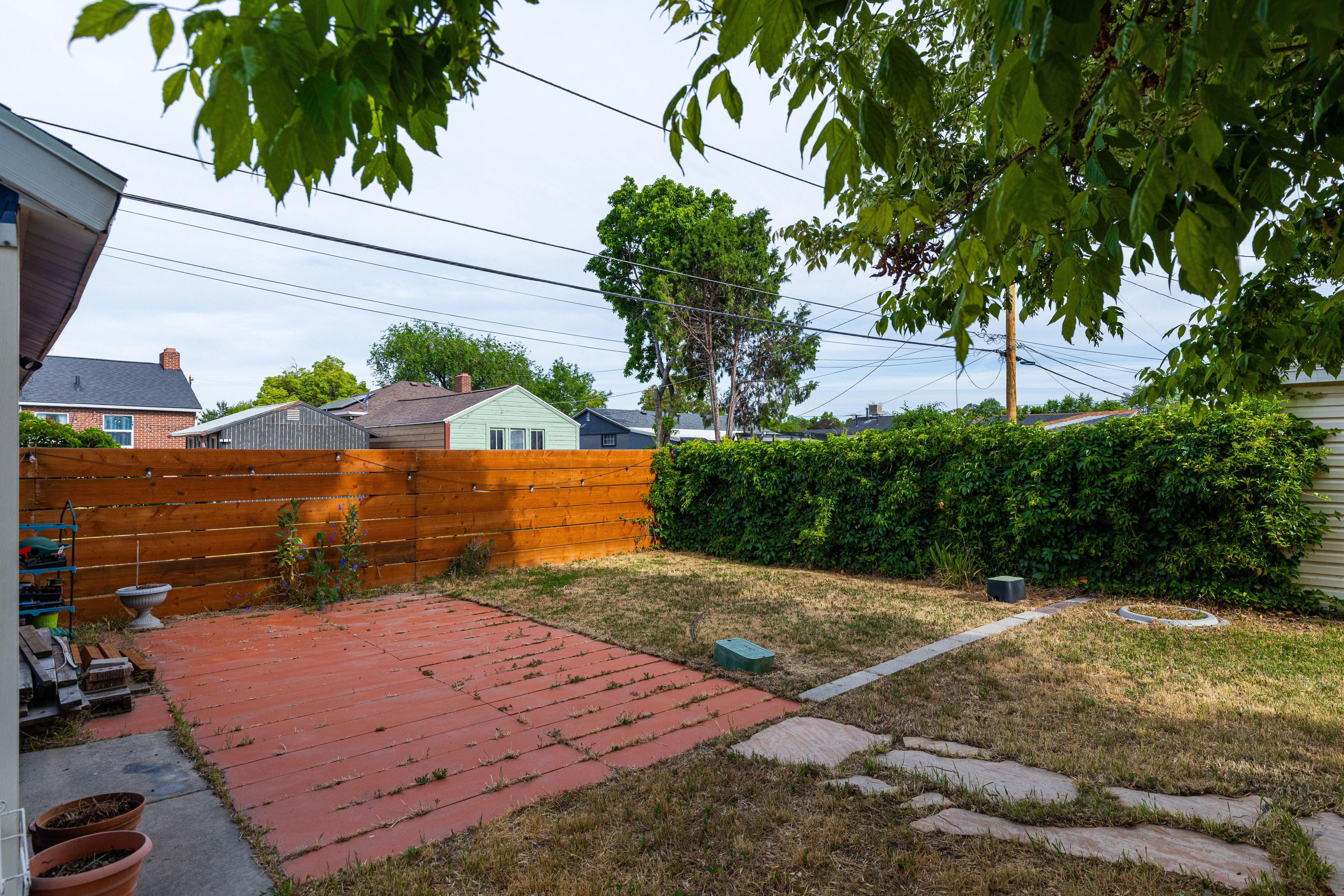 Private backyard featuring a wood privacy fence, a separate ivy-covered fence, a paved patio area, and a stepping stone pathway