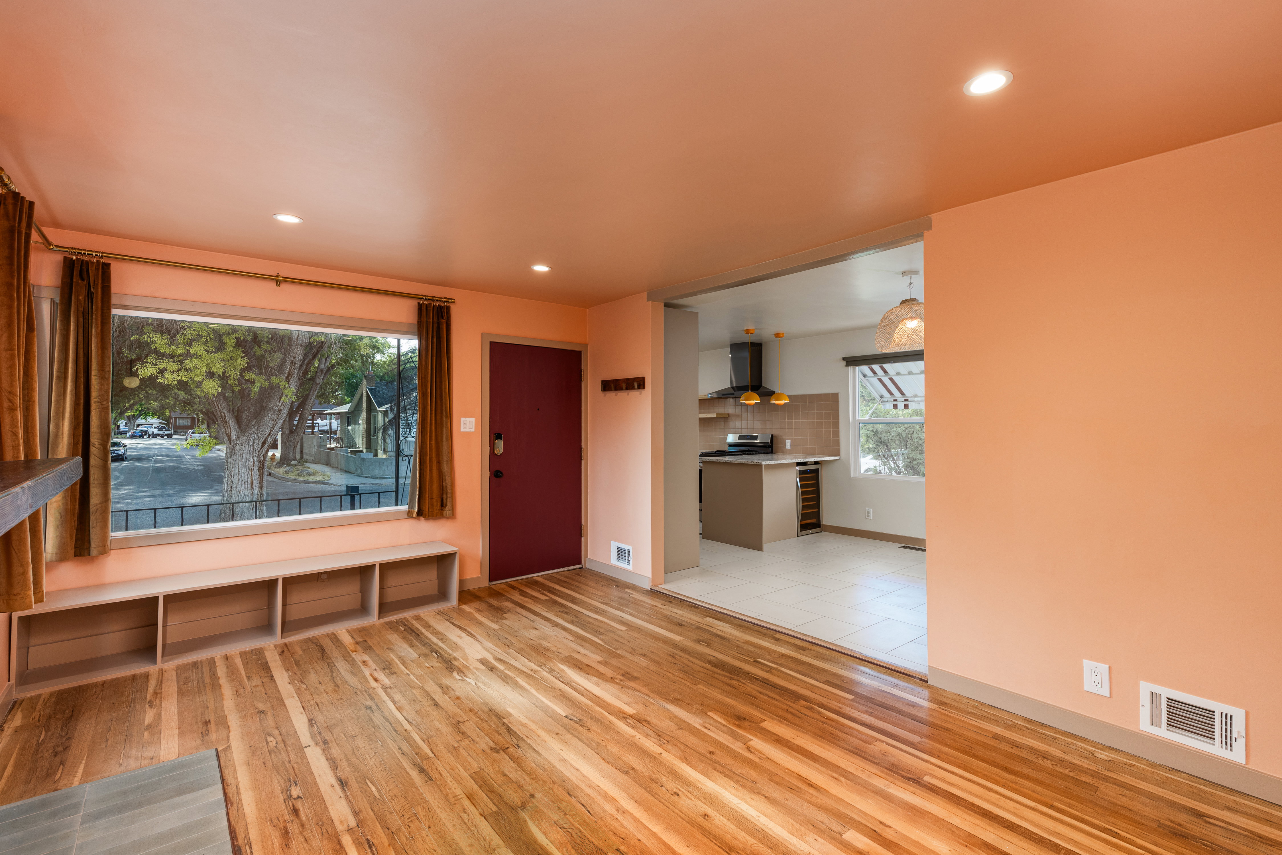 Hardwood flooring throughout the main room, featuring a front entry door, recessed lighting, and a large front window with built-in shelving
