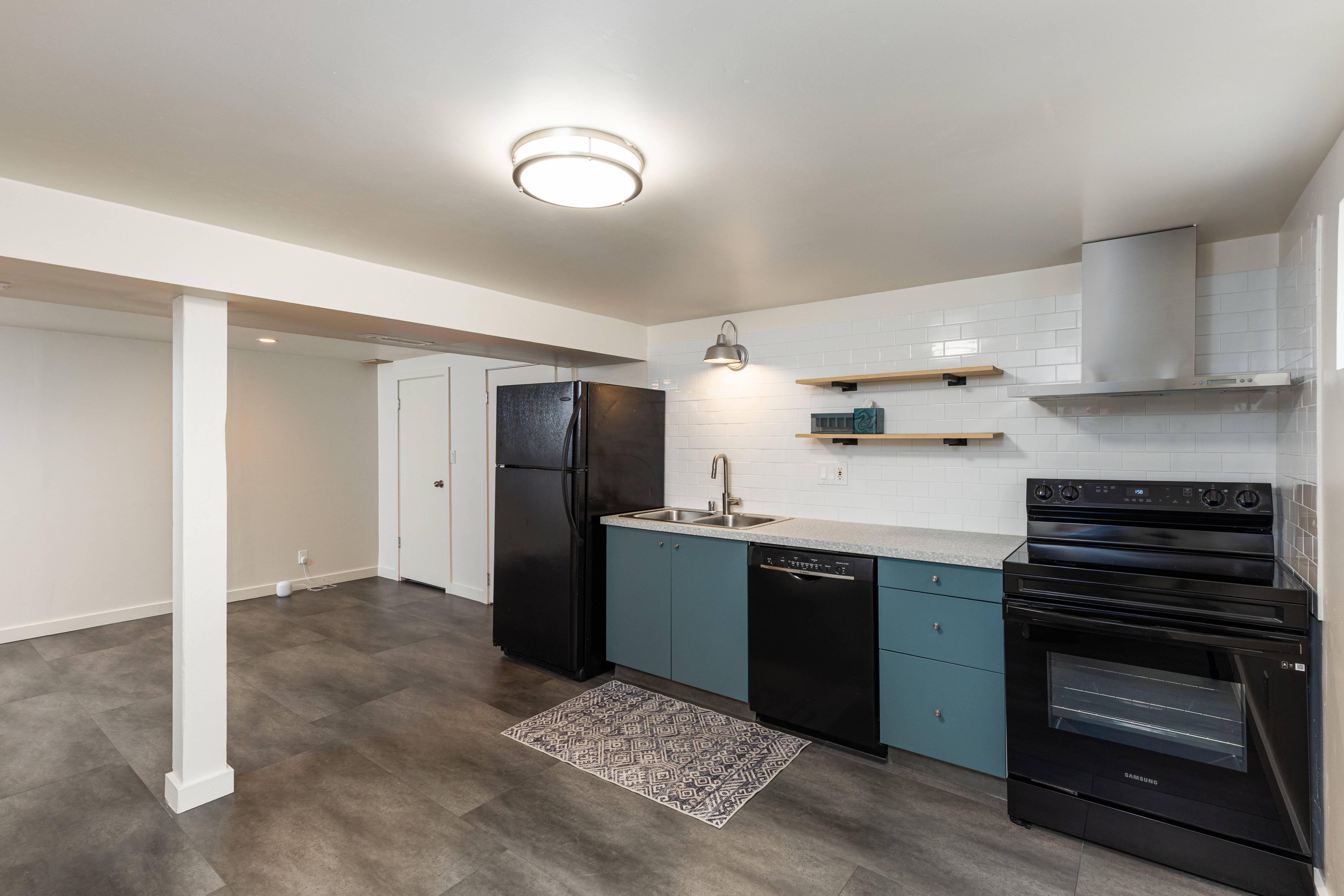 Modern kitchen area featuring wood-finish flooring, subway tile backsplash, teal cabinetry, and stainless steel appliances