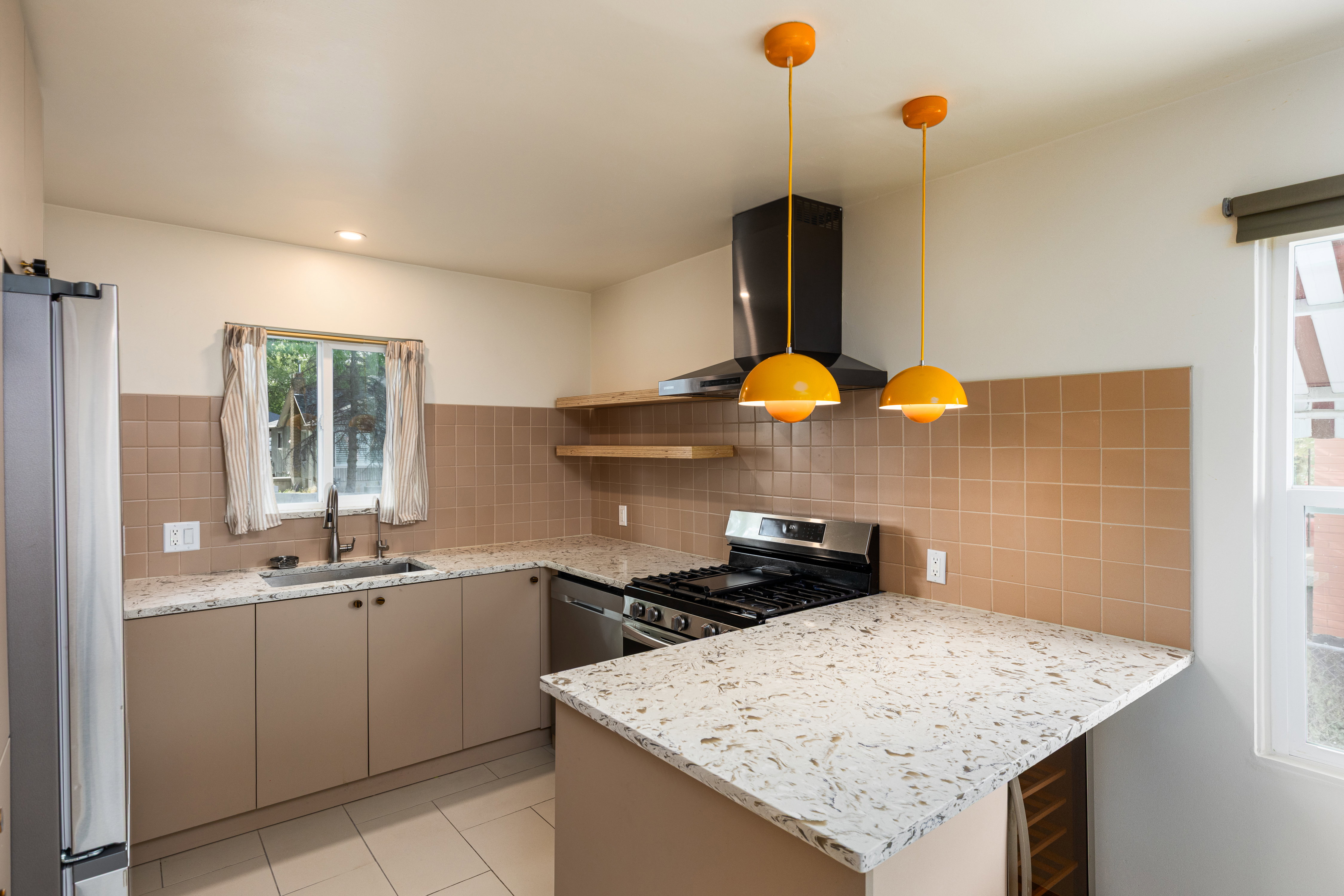 Kitchen featuring light-toned cabinetry, light-colored countertops, square tile backsplash, and stainless steel appliances including a gas range with a matching hood