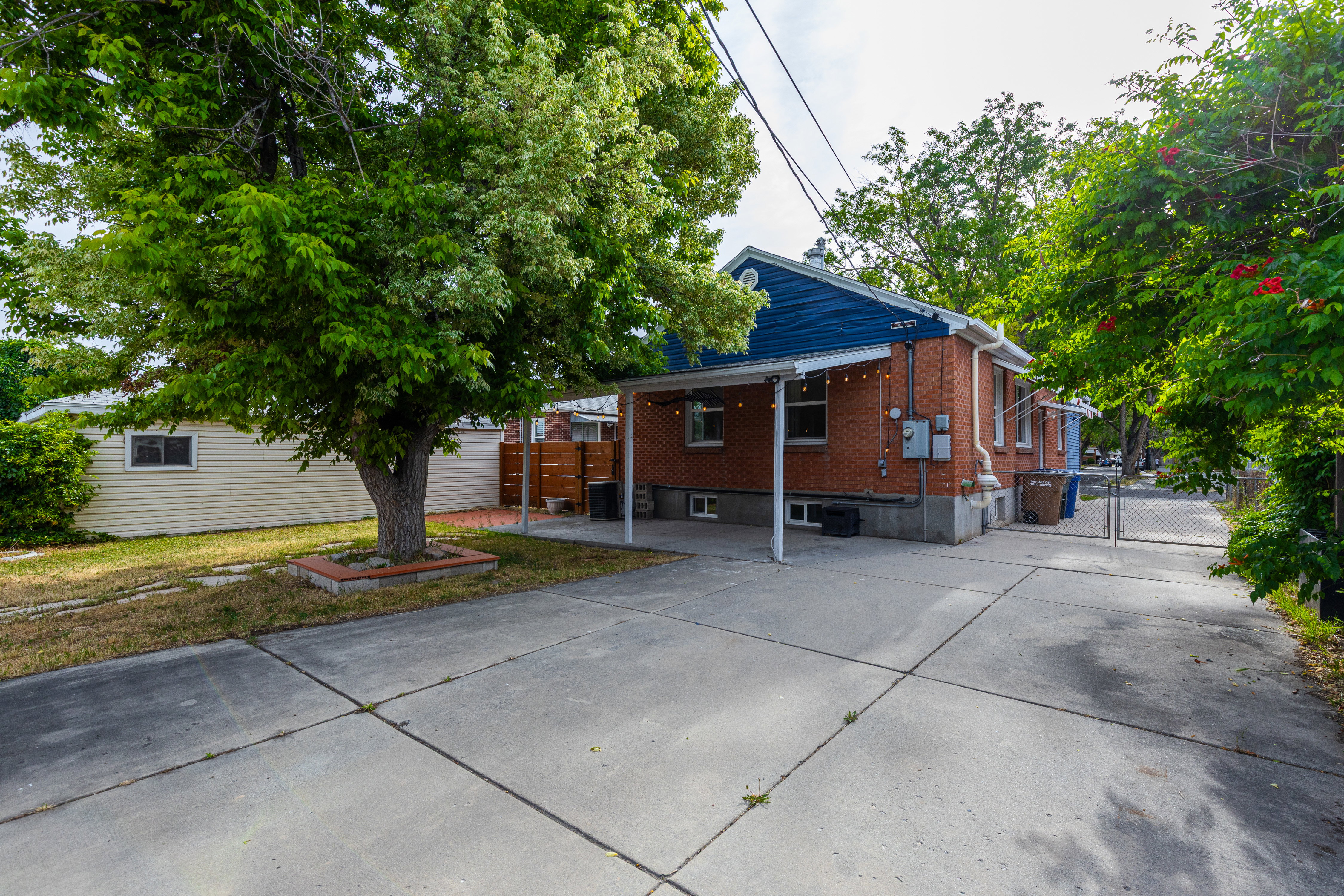 Brick exterior with blue siding accents, featuring a covered concrete patio and a gated concrete driveway