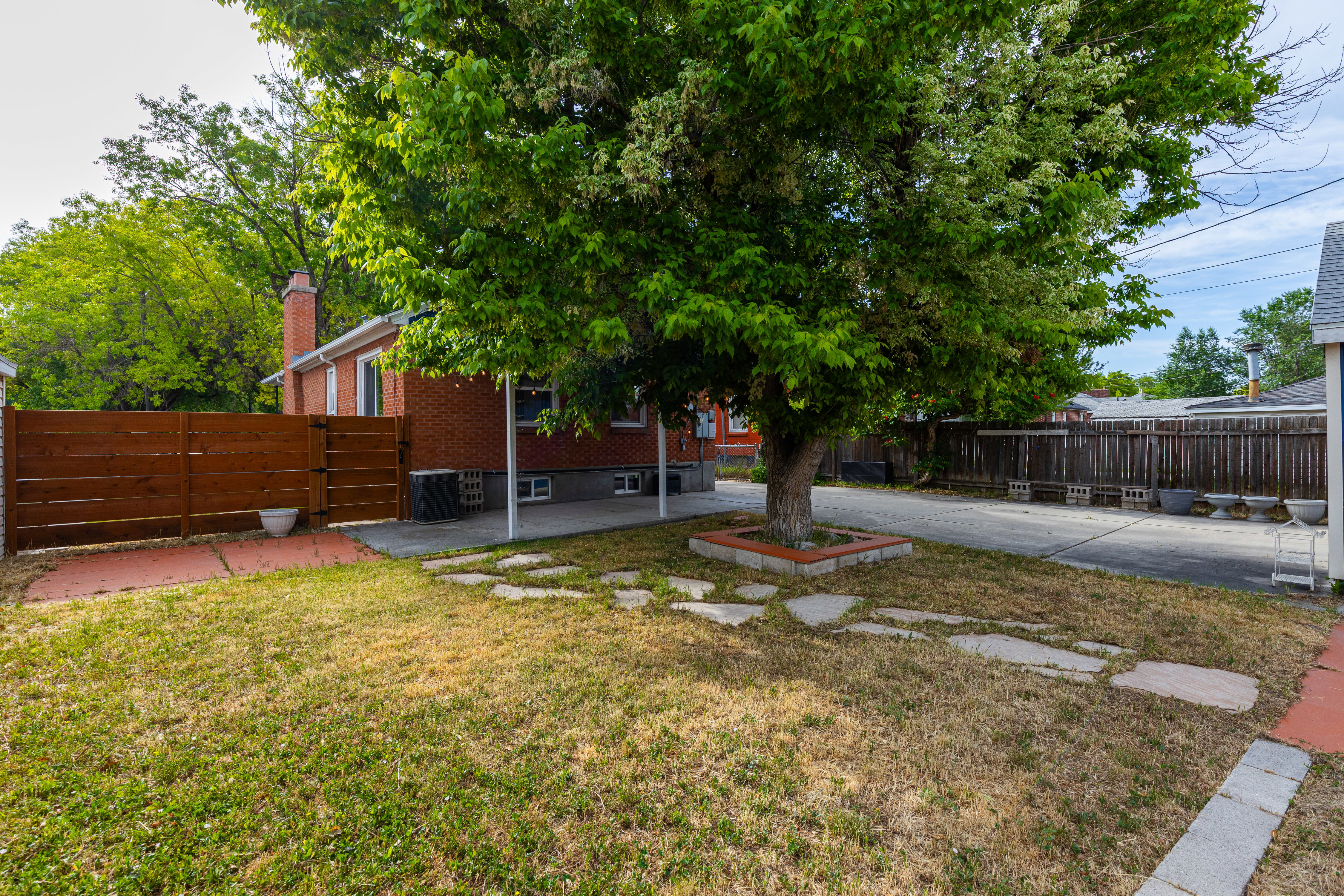 Spacious backyard featuring a large tree, flagstone pathway, and concrete patio area