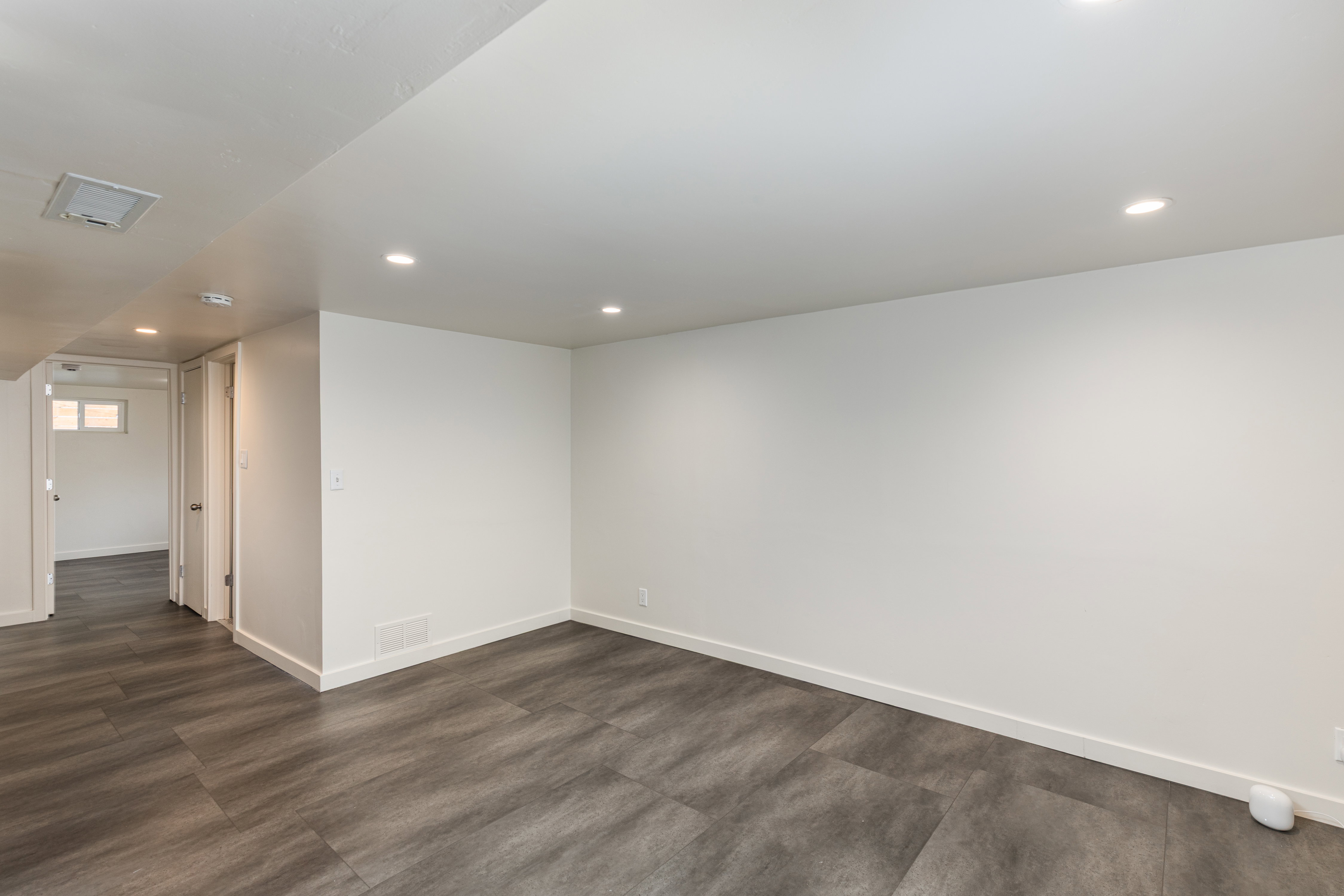 Spacious room featuring wood-finish flooring, recessed lighting, white walls, and white baseboards