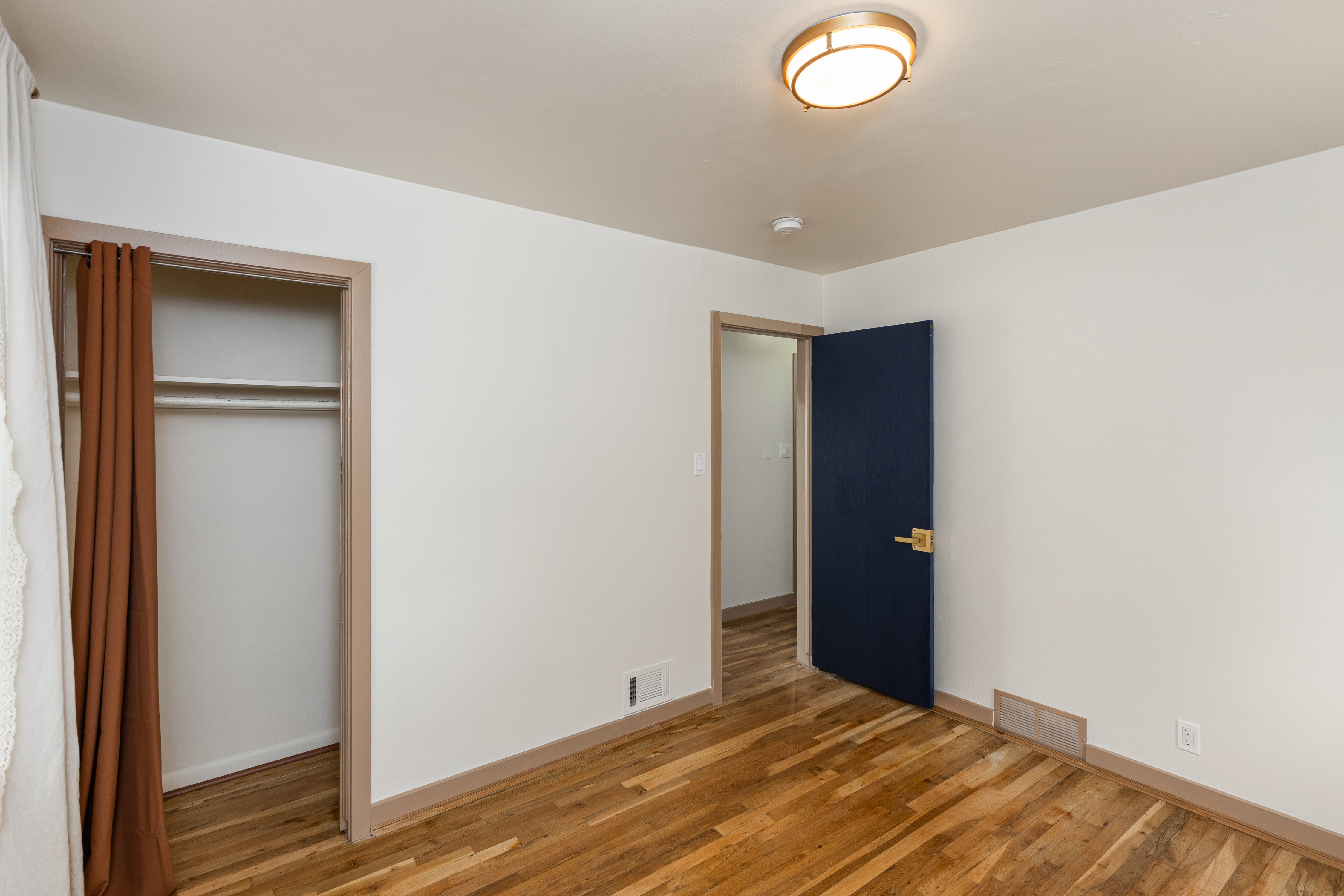 Hardwood flooring throughout featuring white walls, a built-in closet with shelving and hanging rod, and a deep blue door with a brass handle