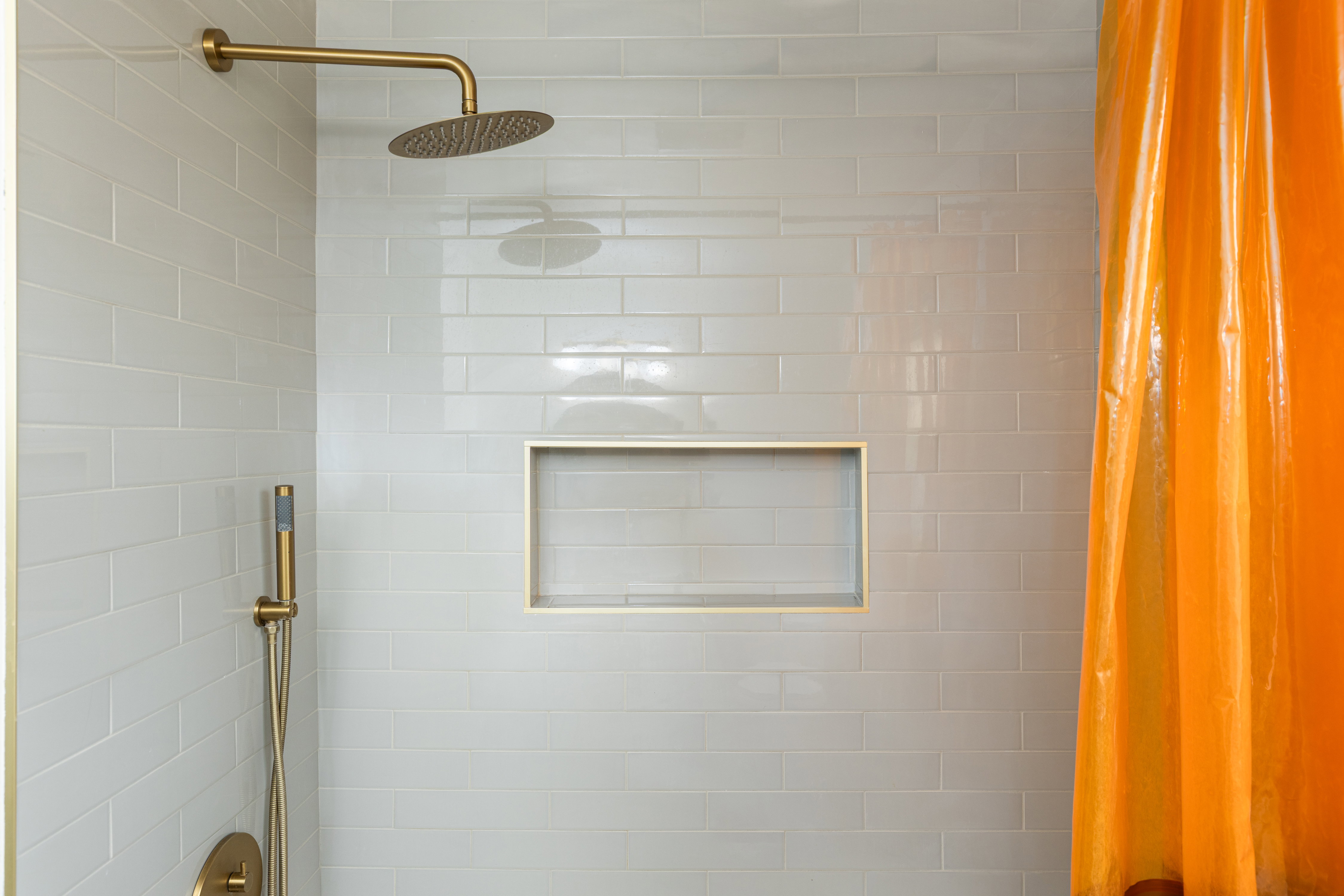 Shower with subway tile surround, featuring a built-in niche, and a gold-finish rain shower head with an accompanying handheld spray