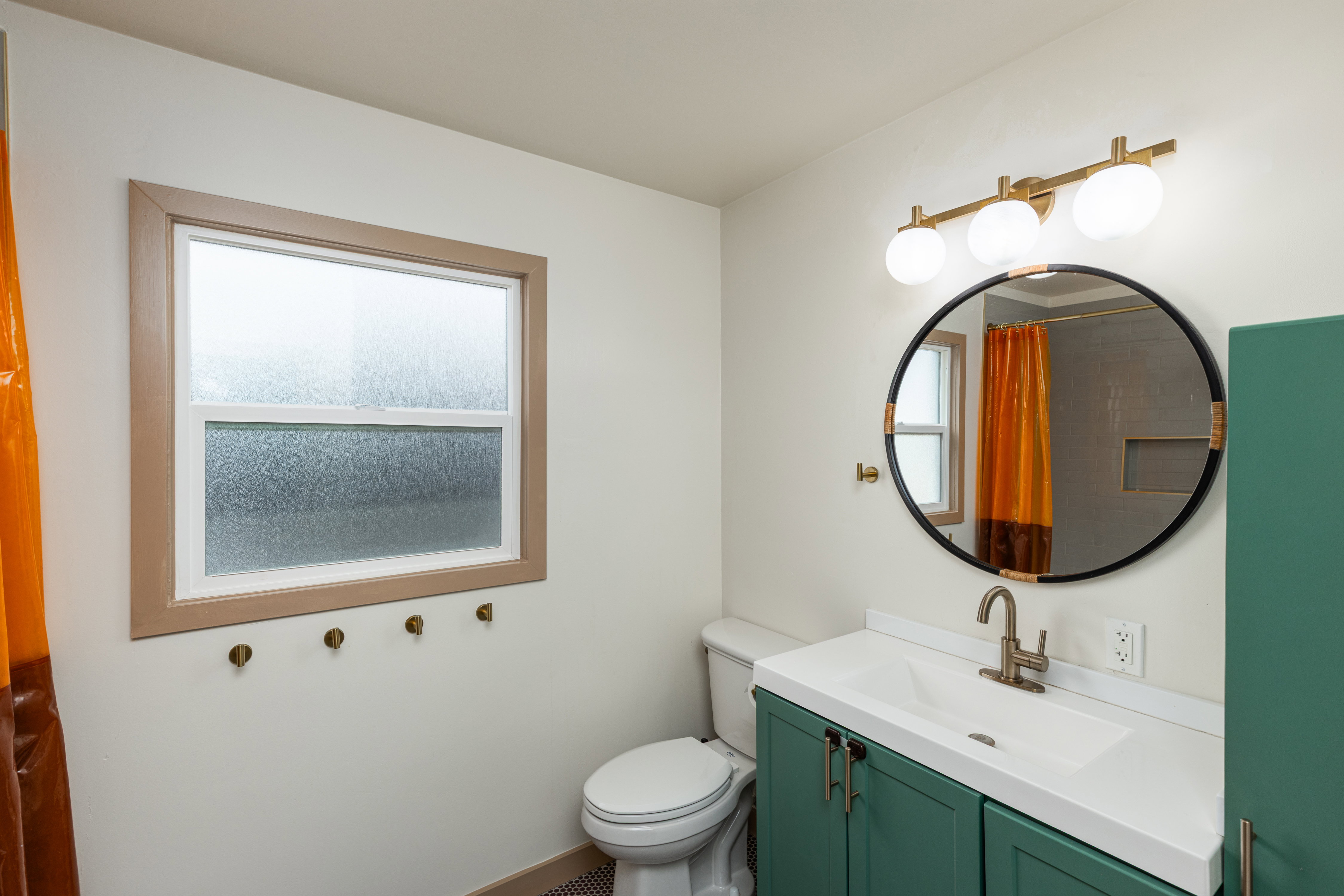 Bathroom featuring a green vanity with white countertop, circular mirror, and brass-finish light fixture