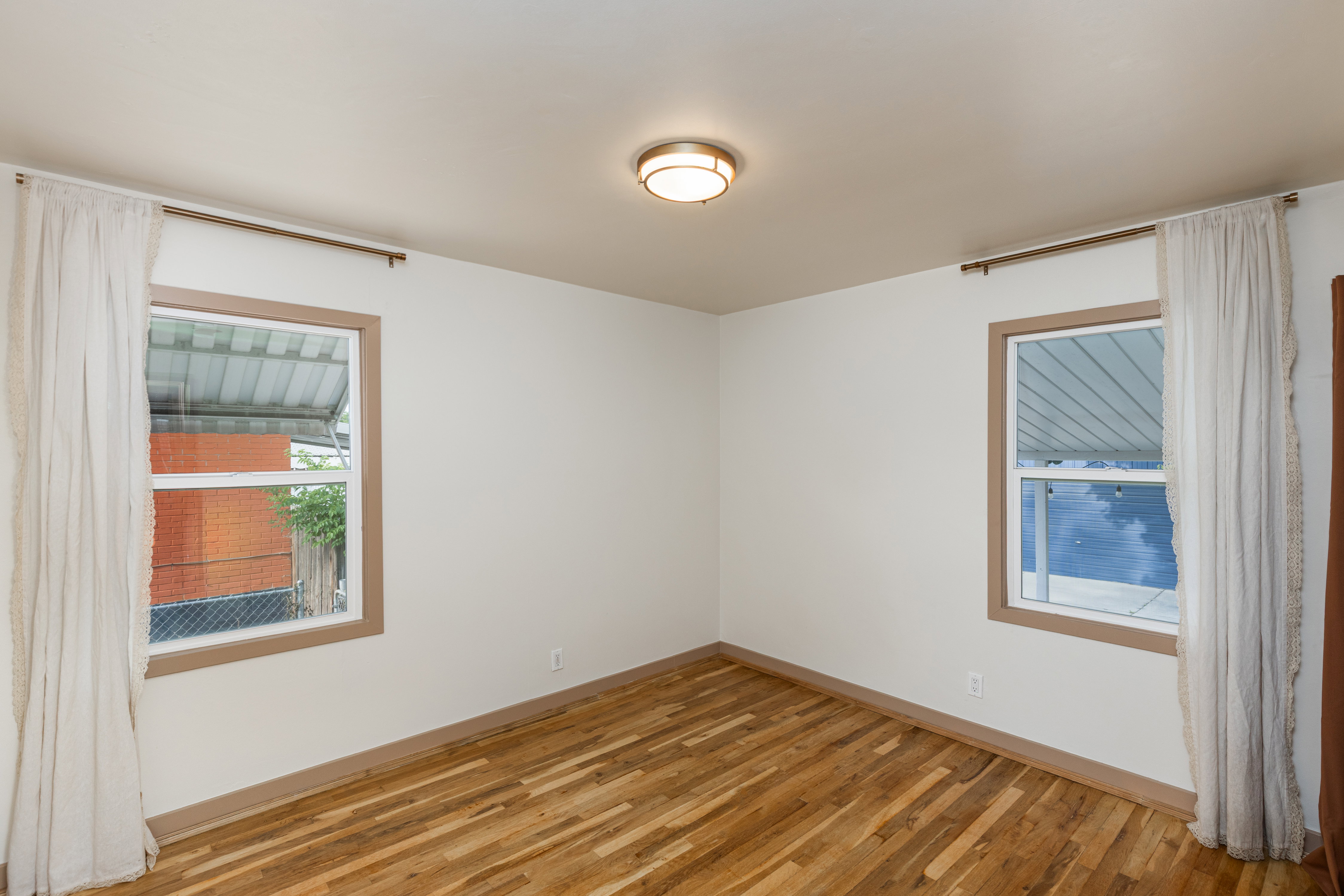 Room featuring wood-finish flooring, two windows with trim, and a flush-mount ceiling light fixture
