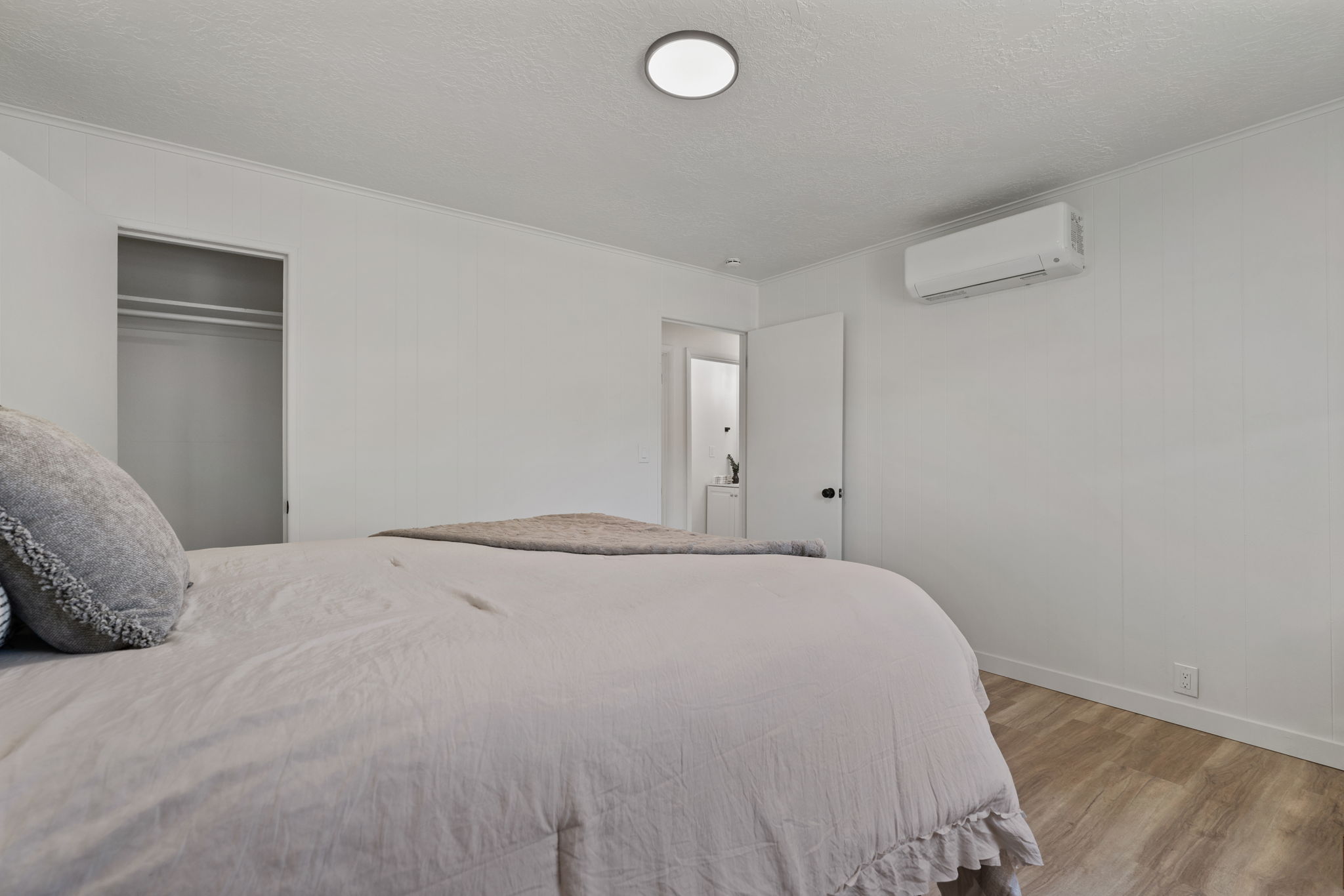 Spacious room featuring light wood-finish flooring, white panel walls, and a mini-split system