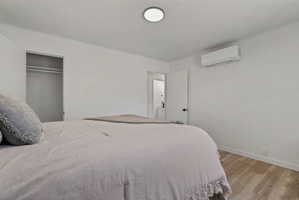 Spacious room featuring light wood-finish flooring, white panel walls, and a mini-split system