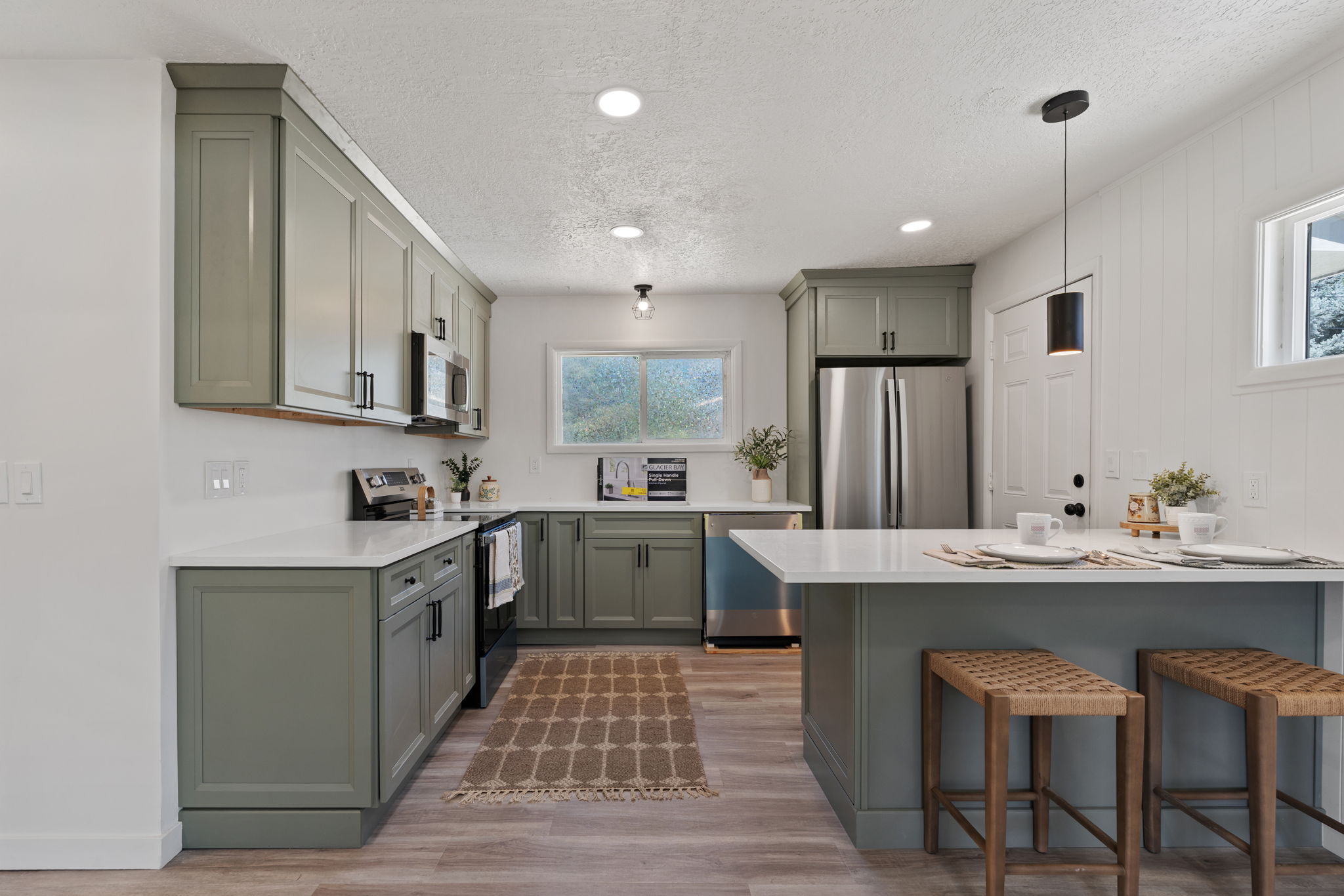 Kitchen featuring sage green cabinetry, white quartz countertops, stainless steel appliances, and light wood-finish flooring