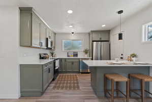 Kitchen featuring sage green cabinetry, white quartz countertops, stainless steel appliances, and light wood-finish flooring