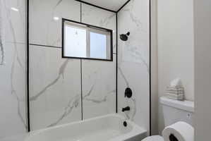 Bathtub and shower combination featuring white marble-look paneling with black trim, a black-framed window, and matte black fixtures