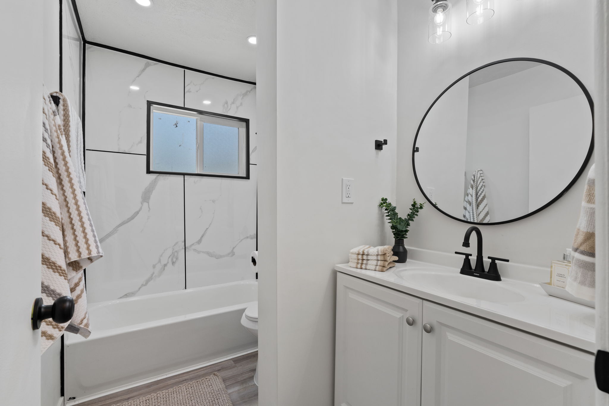 Contemporary bathroom featuring a white vanity with integrated sink, black-framed oval mirror, and matte black fixtures