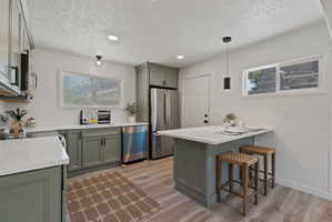 Updated kitchen featuring sage green cabinetry, white countertops, stainless steel appliances, wood-finish flooring, and a central island with seating